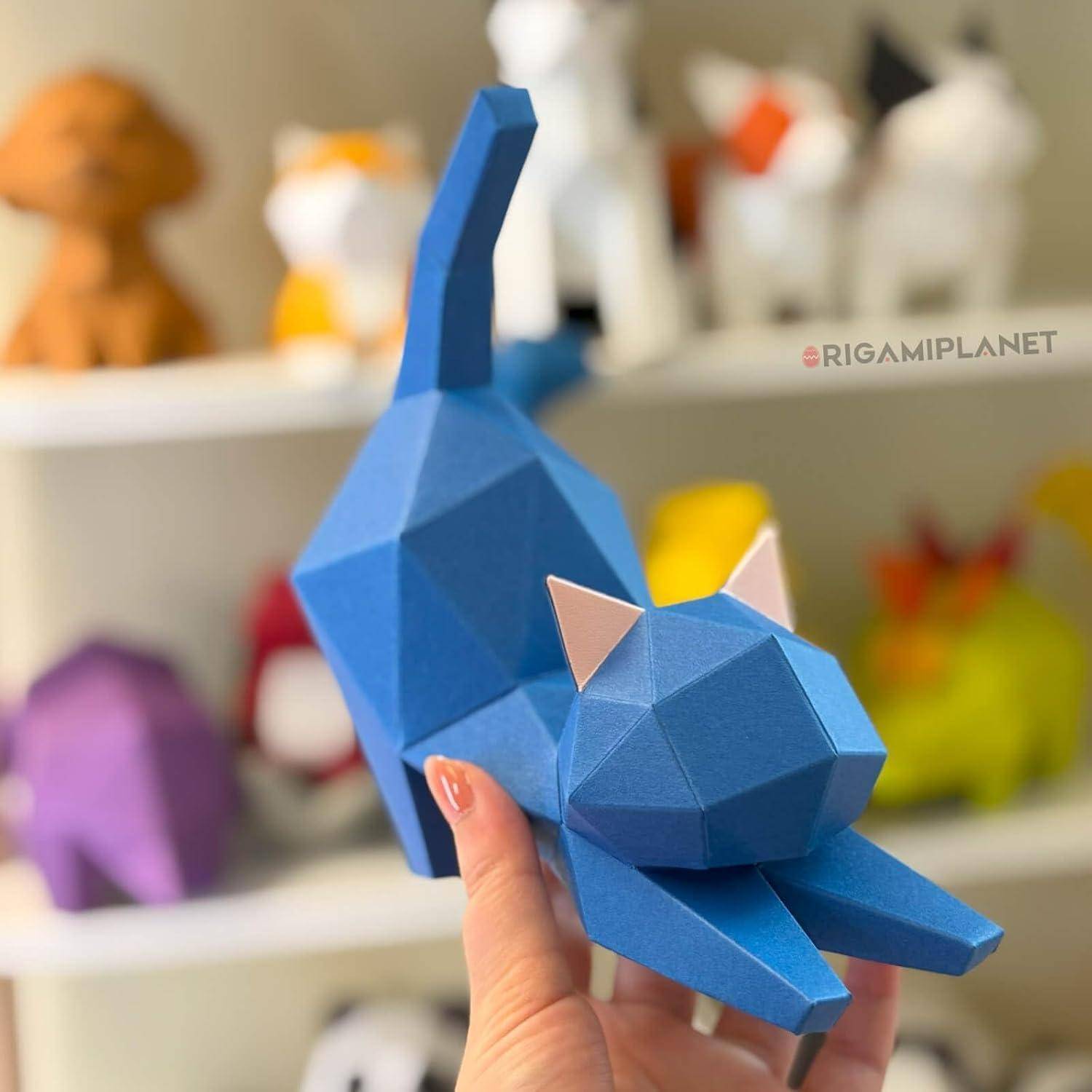 Hand hält eine blaue facettierte geometrische Katzenfigur, mit bunten Tiermodellen unscharf auf Regalen im Hintergrund.