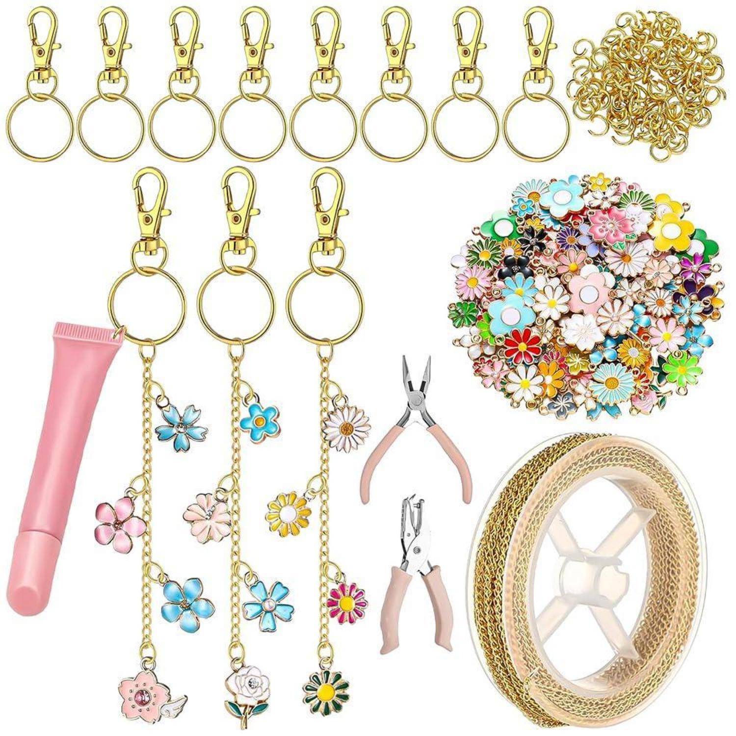 Bastelzubehör-Set mit goldenen Schlüsselanhängern, Sprungringe, Blumencharms, rosa Werkzeuggriffe und dekorative Bandrolle.