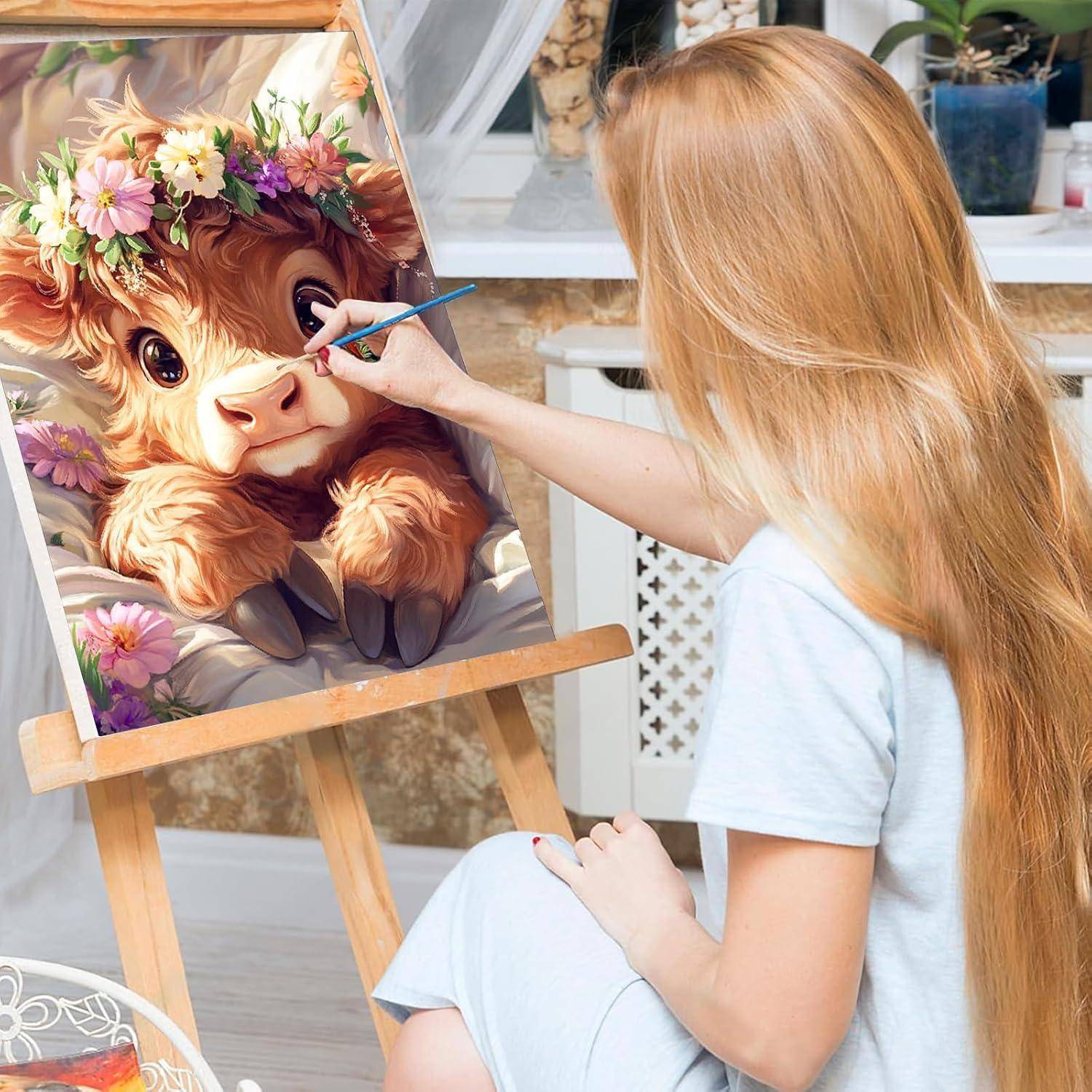 Eine Frau malt auf einer Staffelei ein niedliches Porträt eines Kalbes mit Blumenkrone in einem hellen Studio.