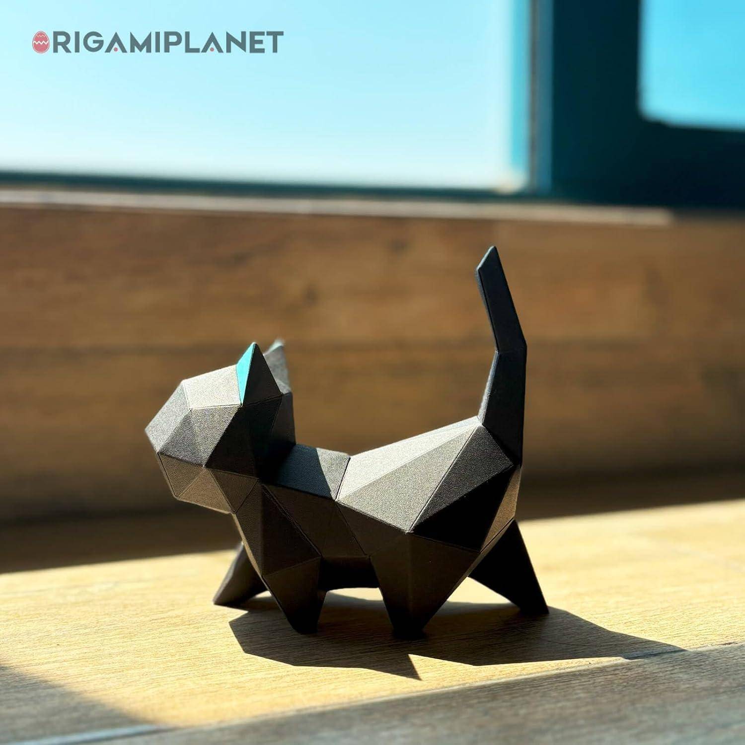 Eine geometrische schwarze Origami-Stil Katzenfigur steht auf einer sonnenbeschienenen Holzoberfläche in der Nähe eines Fensters.
