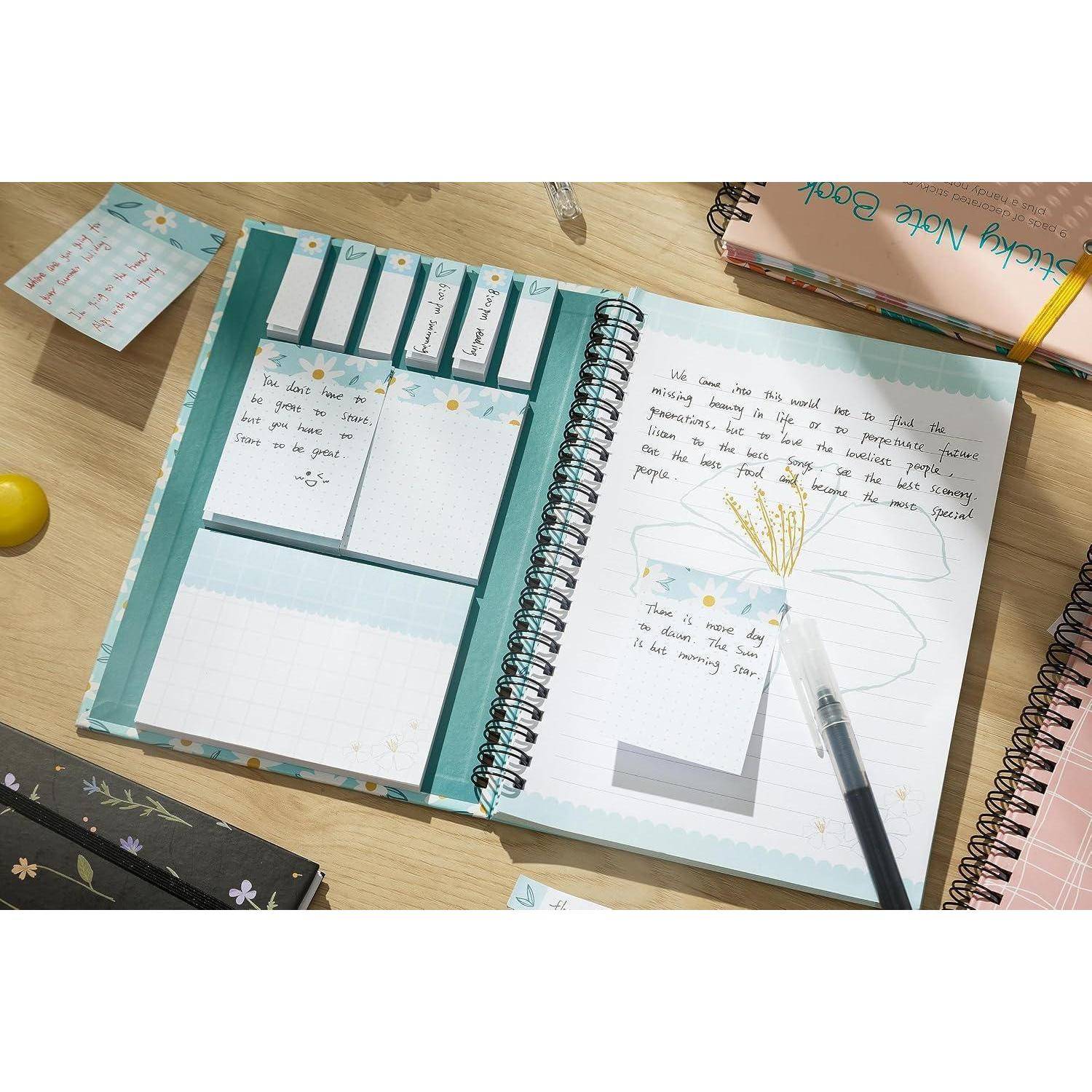 Offenes Spiralnotizbuch mit eingeklebten Notizseiten und handschriftlichen Tagebucheinträgen auf einem Schreibtisch, umgeben von Schreibwaren und einem Stift.