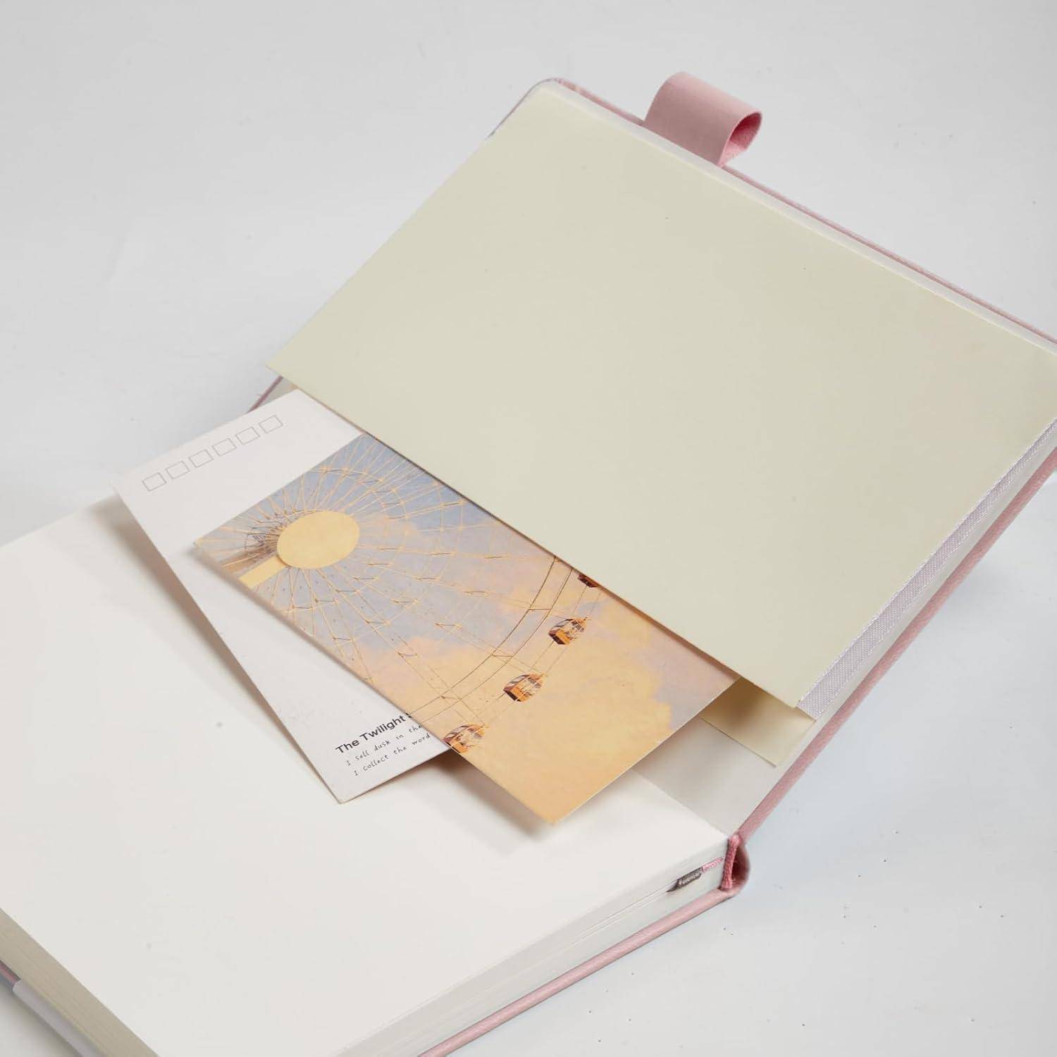 Aufgeschlagenes rosa Notizbuch oder Planer mit cremefarbenem Einband und leeren Seiten, in das zwei kleine Fotokarten teilweise hineingesteckt sind.