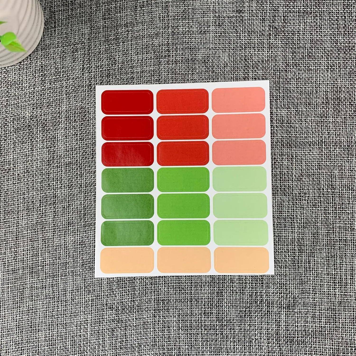 Ein Farbmusterchart mit Reihen von roten, grünen und pfirsichfarbenen abgerundeten Rechtecken auf einer weißen Karte, die auf einer grauen Stoffoberfläche liegt.