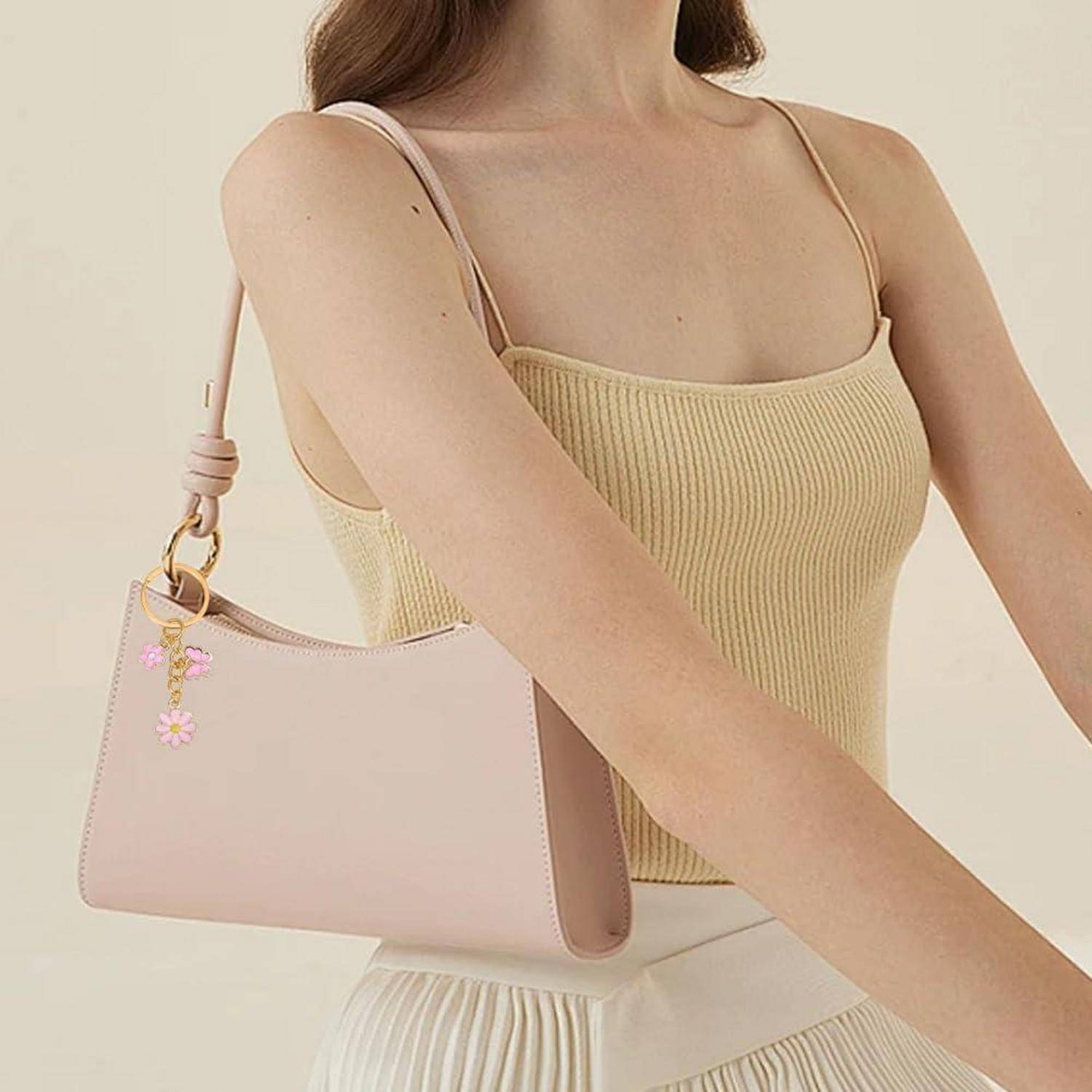 Eine Frau trägt ein beiges geripptes Oberteil und trägt eine errötendrosa Schultertasche mit einem kleinen Blumenschmuck.