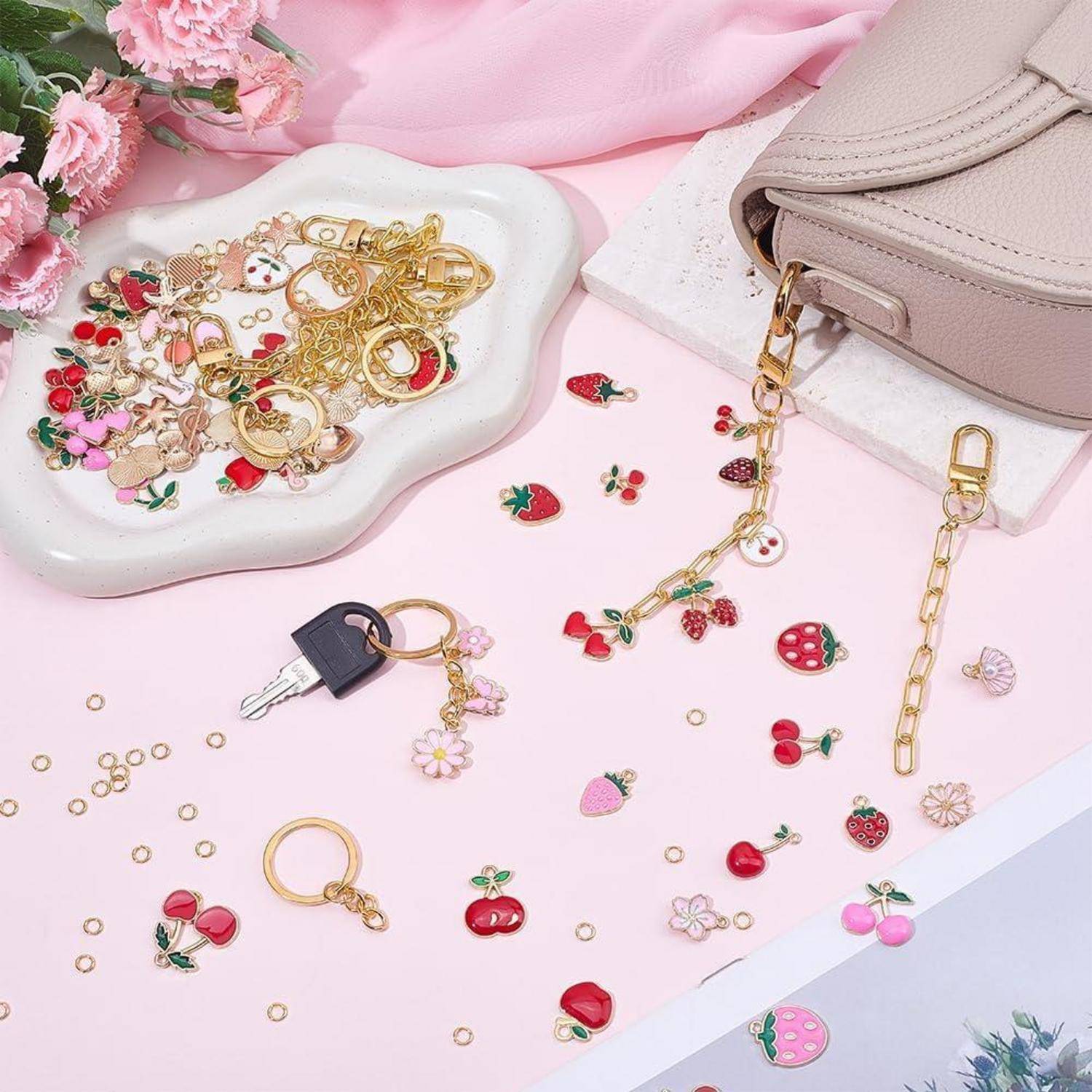 Eine rosa Handtasche und ein Schmuckständer mit goldenen Schlüsselanhängern und bunten Obst- und Blumenverzierungen, verstreut auf einer pastellrosa Oberfläche.