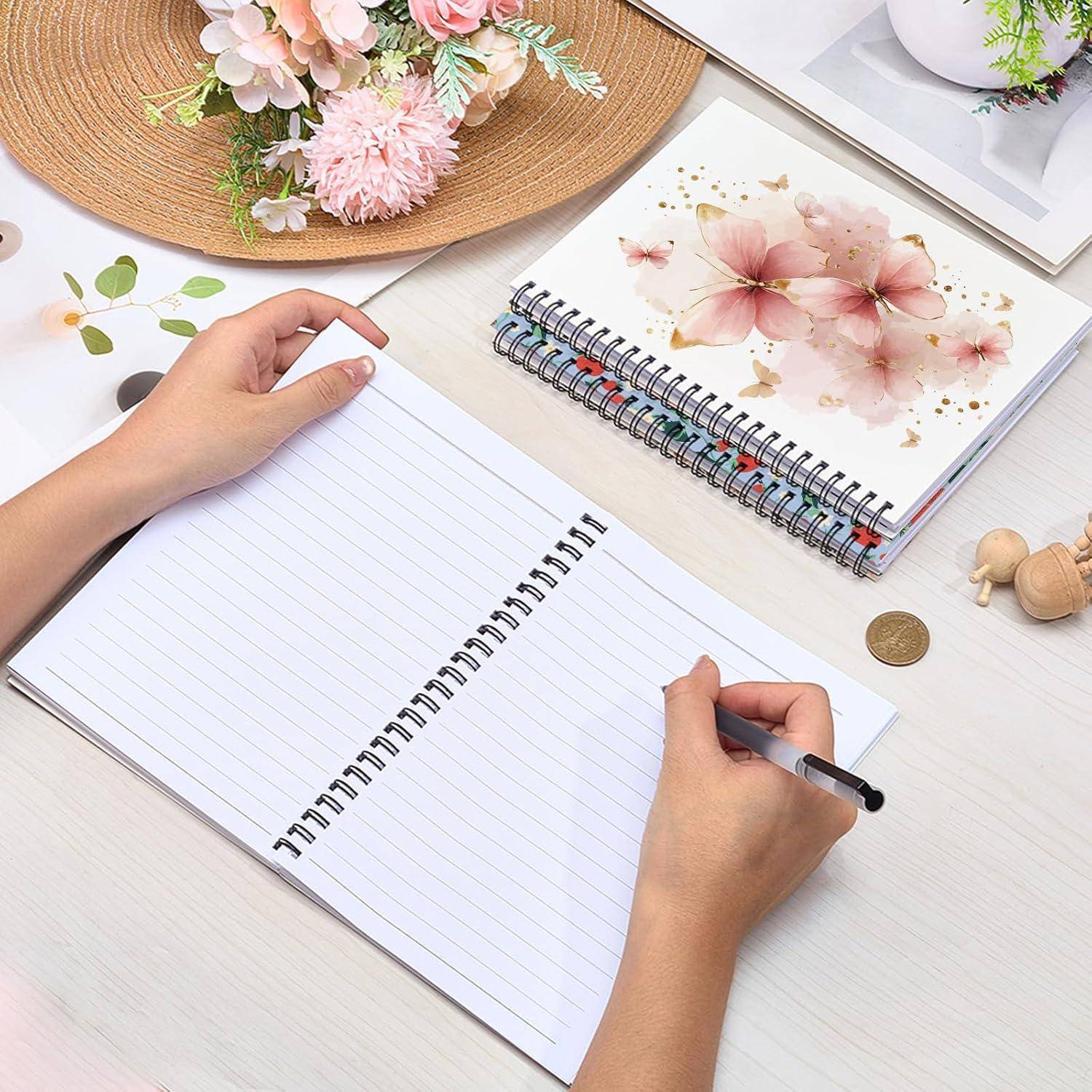 Hände, die in einem linierten Notizbuch auf einem Schreibtisch schreiben, neben einem Blumenspiralblock, Blumen, Münzen und einem Strohhut mit Blüten.