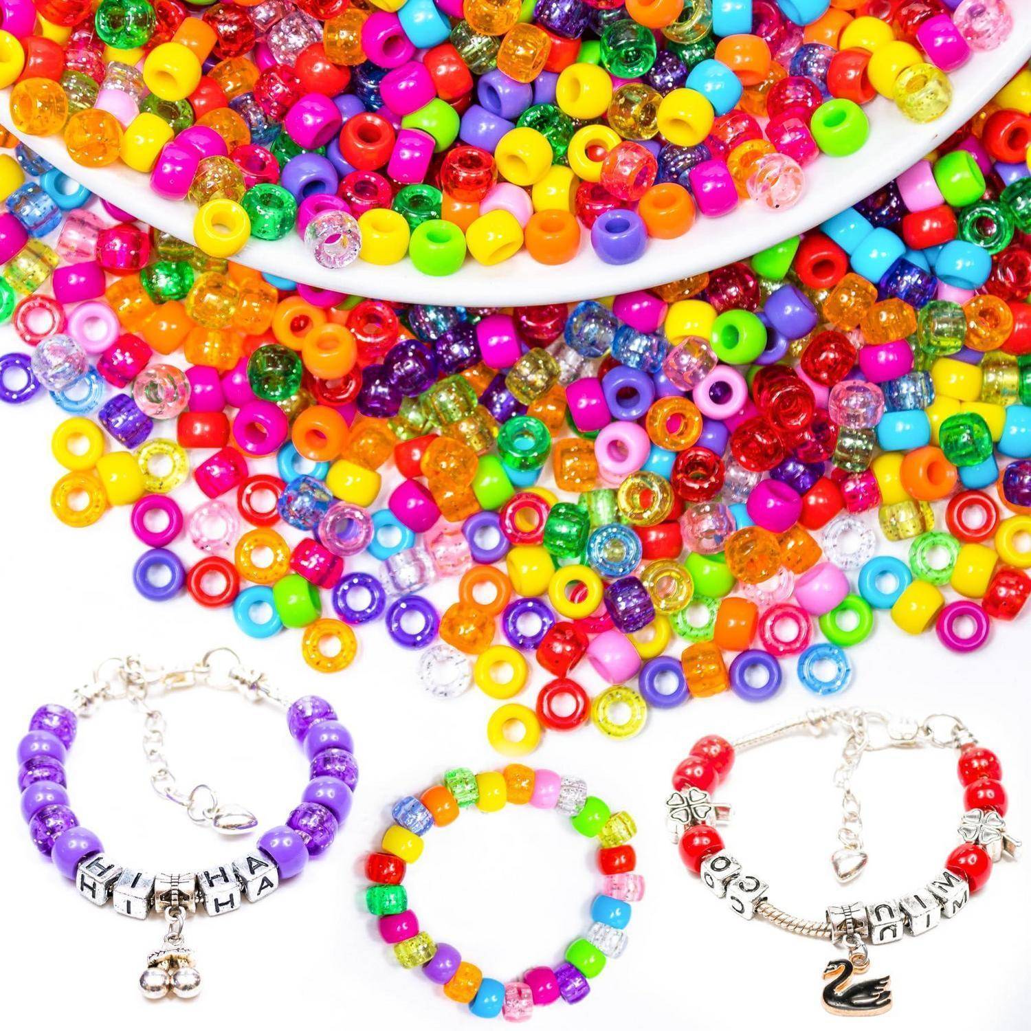 Bunte Kunststoff-Saatperlen verschütten sich aus einer weißen Schale, darunter drei Perlenbänder mit Buchstabenperlen und kleinen Charms.