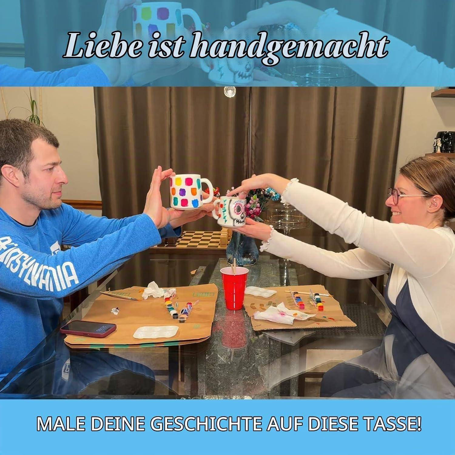 Ein Mann und eine Frau malen zusammen und halten Tassen an einem Tisch, mit deutschem Text: „Liebe ist handgemacht" und „Male deine Geschichte auf diese Tasse!"