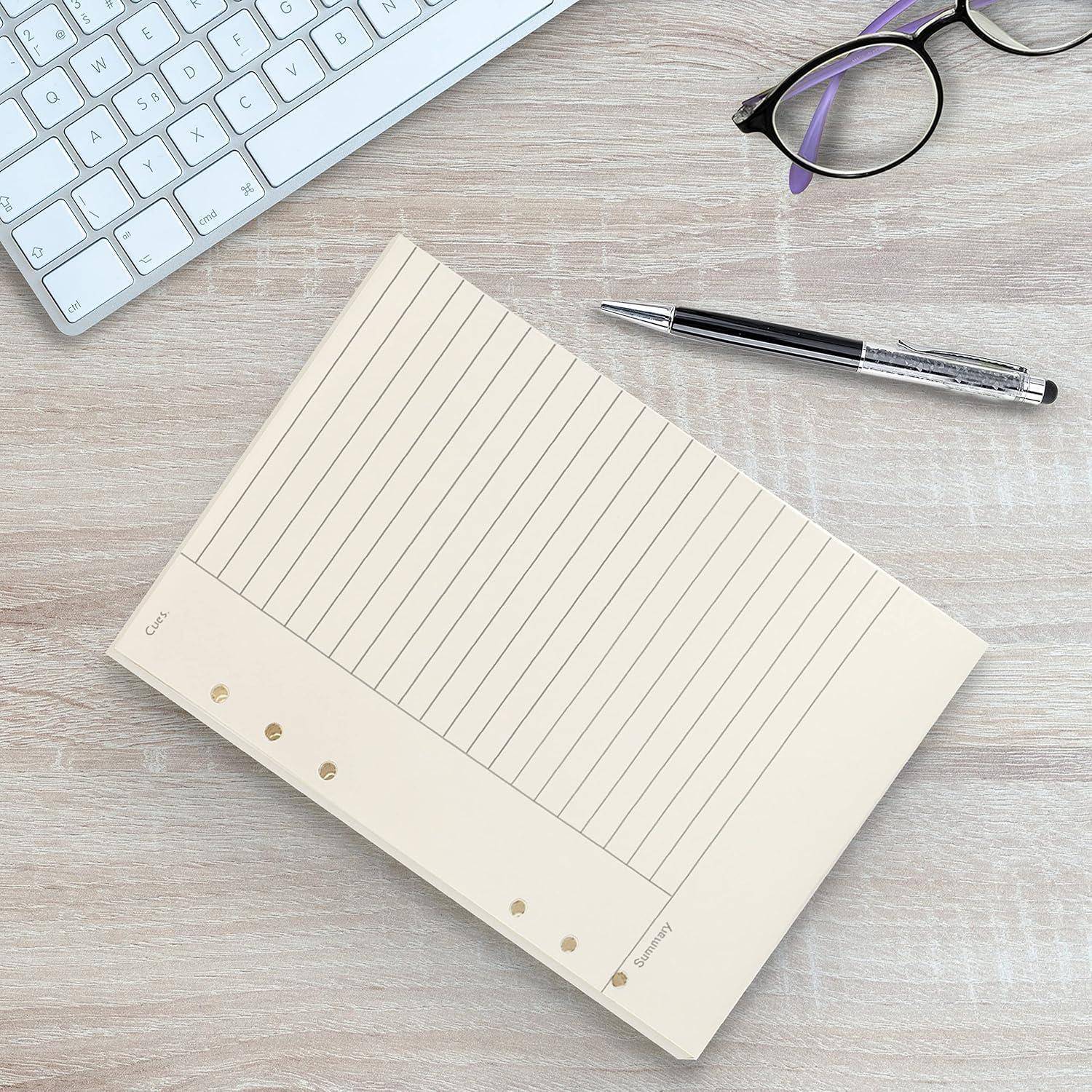 Draufsicht auf ein liniertes Notizbuch neben einer Tastatur, einem Stift und einer Brille auf einer hellen Holzoberfläche.