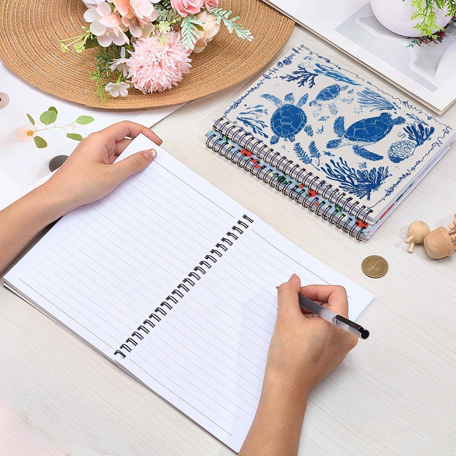 Hände schreiben in einem leeren Spiralblock auf einem ordentlichen Schreibtisch neben einem Notizbuch mit blauem Schildkrötenmuster, Blumen und einer Münze.