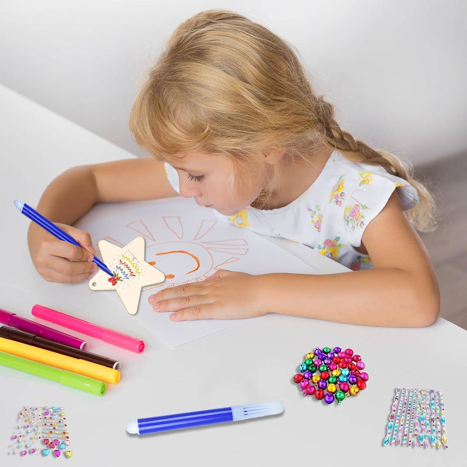 Junges Mädchen, das ein sternenförmiges Kunsthandwerk mit Markern an einem weißen Tisch verziert, umgeben von bunten Kunstmaterialien und Strass-Stickern.