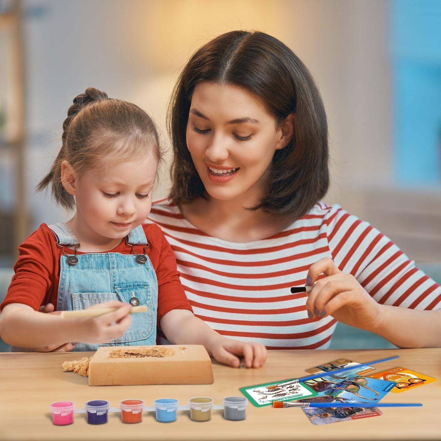 Mutter und kleine Tochter malen und spielen an einem Tisch mit Bastelmaterialien und Bildkarten, was auf eine kreative Lernaktivität hindeutet.