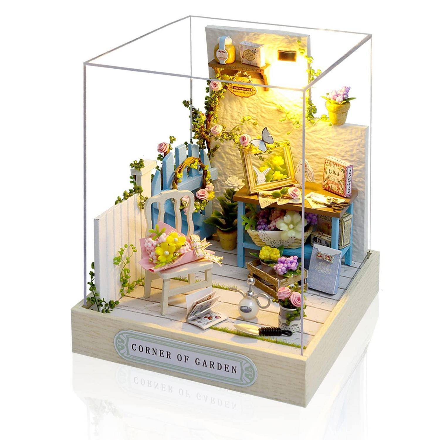 Miniatur-Garten-Diorama in einer klaren Ausstellungsbox mit einem Stuhl, Arbeitstisch, Blumen, Ranken und einem Schild mit der Aufschrift „GARTENECKE