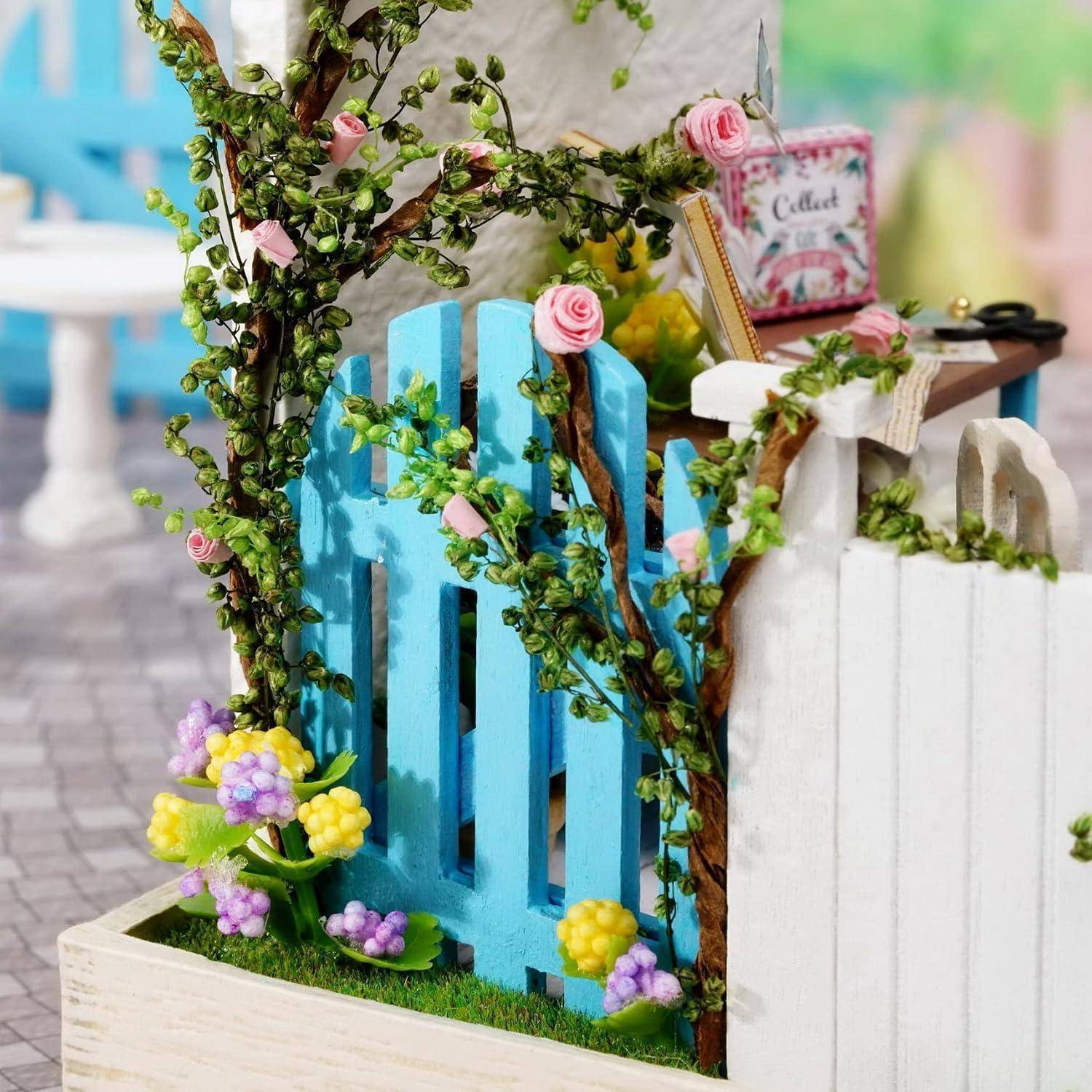 Miniatur-Gartenszene mit blauen und weißen Lattenzäunen, rosa Blumen, Ranken und einem kleinen 