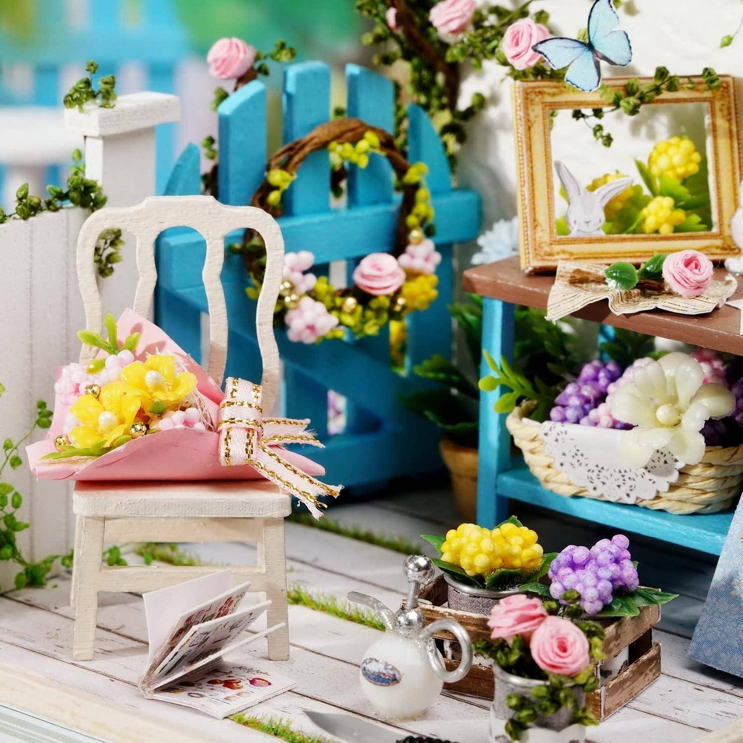 Miniatur-Blumenzimmer mit einem weißen Stuhl, der einen rosa Blumenstrauß hält, blaues Zaun und Regale, Körbe mit Blumen, gerahmte Vogelkunst und eine Teekanne.