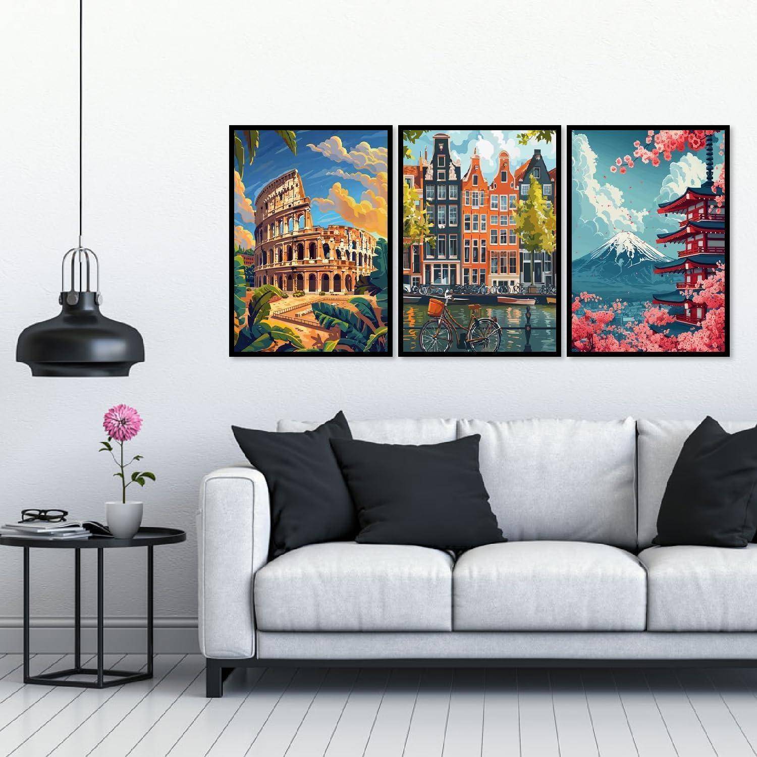 Modernes Wohnzimmer mit weißem Sofa, schwarzen Kissen, hängender Lampe, Beistelltisch mit Blume und drei gerahmten Kunstdrucken im Reisestil mit Stadt- und Landschaftsmotiven über dem Sofa.