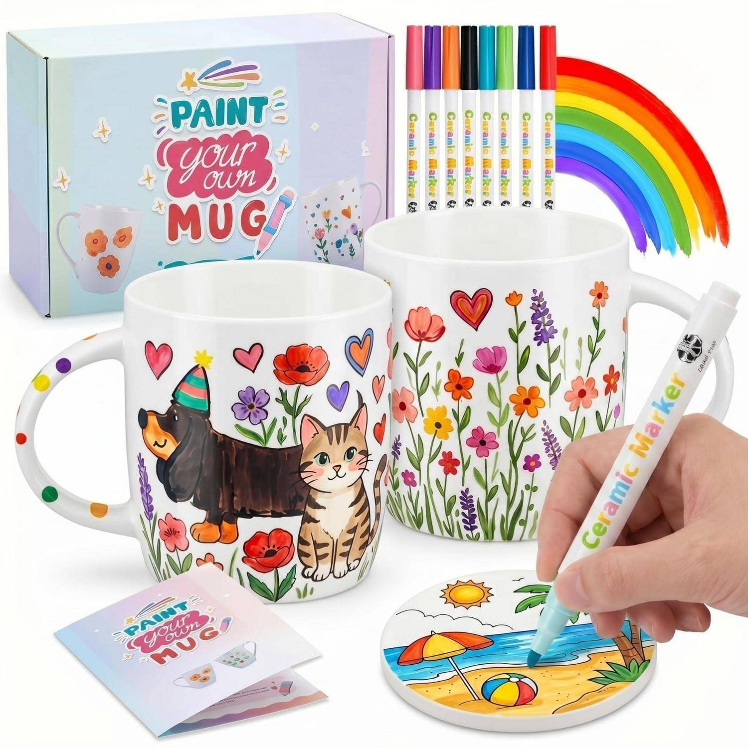 Bemale-deine-eigene-Tasse-Set mit zwei dekorierten Tassen, sechs farbigen Markern, einer Palettenkarte und einer Hand, die eine Untersetzerszene bemalt