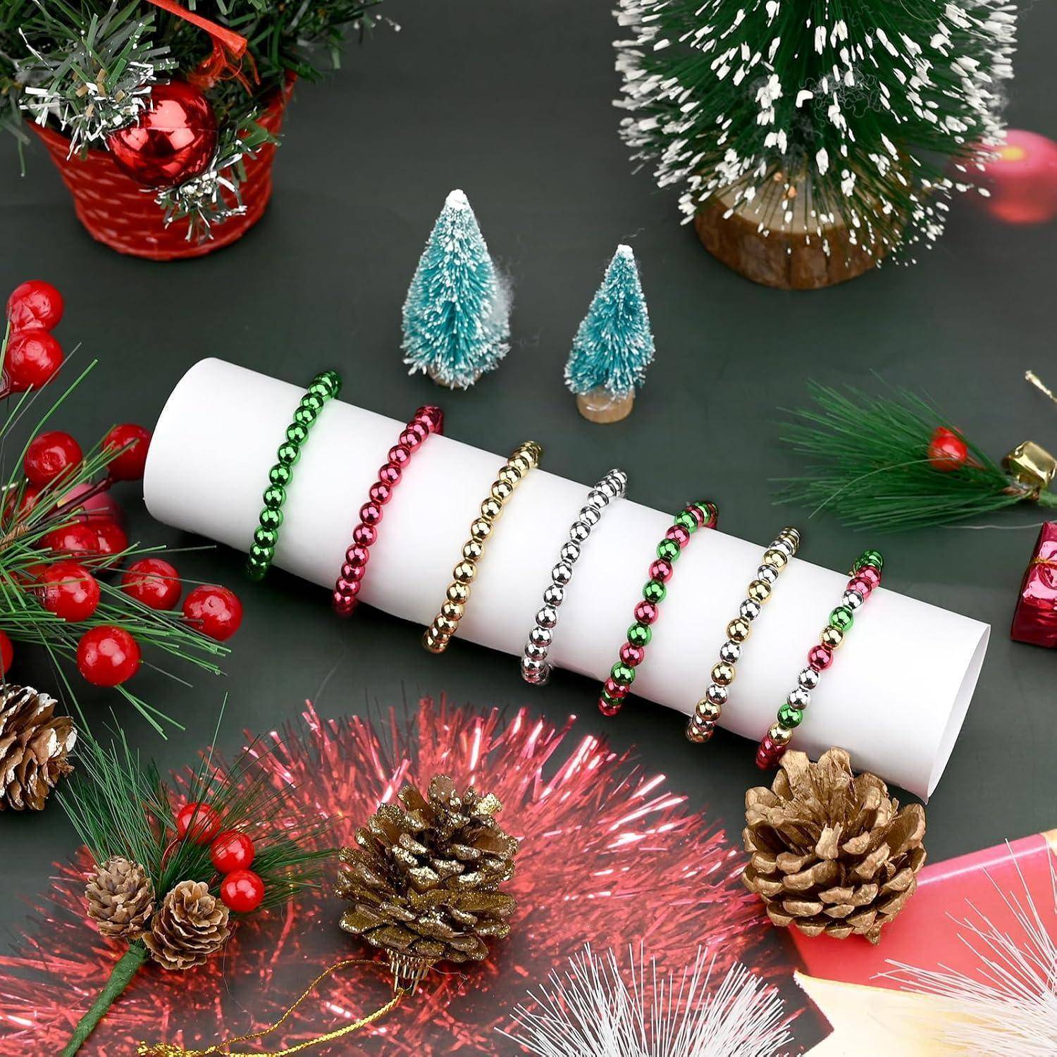 Weißer Displayzylinder mit farbenfrohen Perlenbändern, umgeben von festlichen Weihnachtsdekorationen, Tannenzapfen, Lametta und Miniaturbaumen.