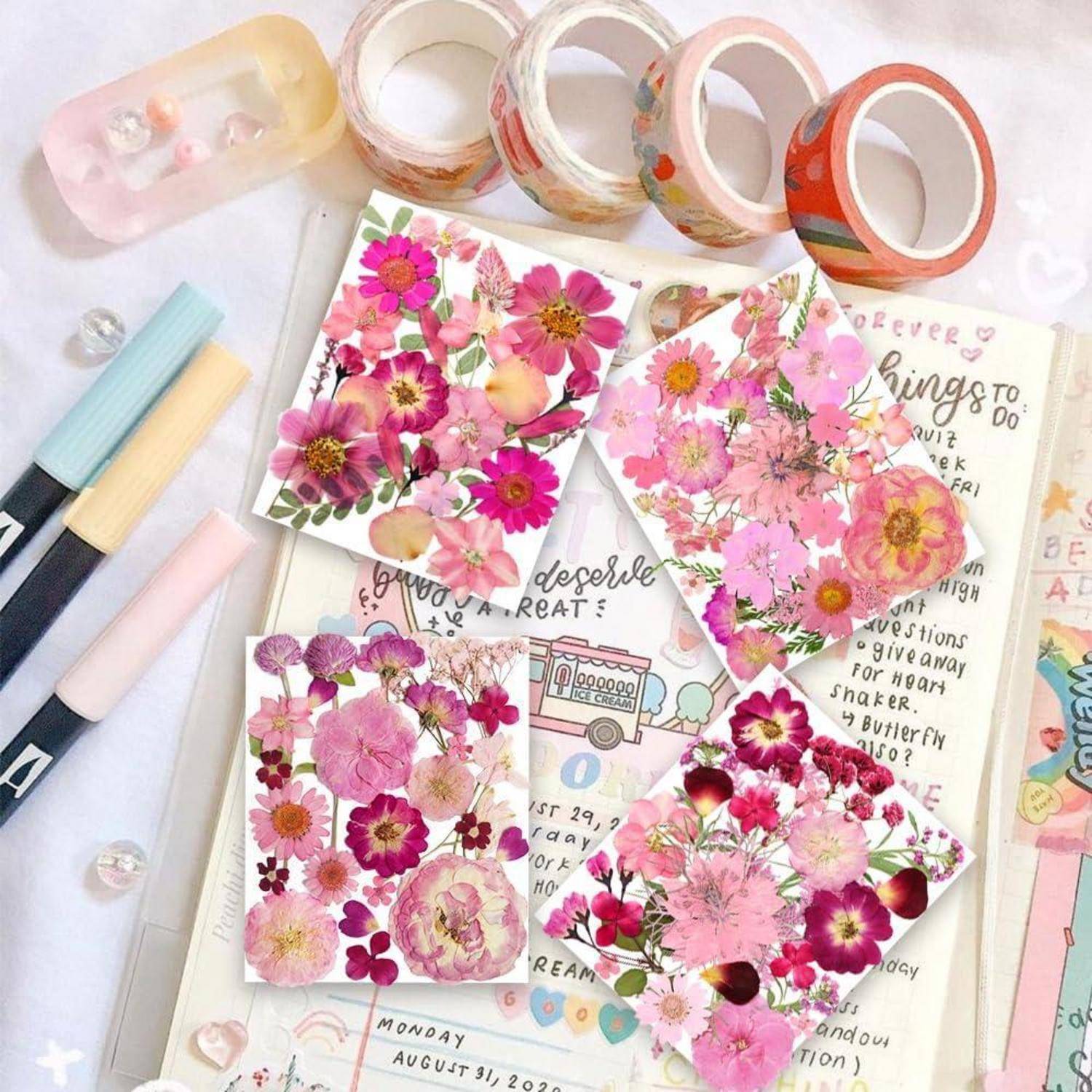 Dekoratives Schreibwarenleayout mit rosa Blumencollage-Karten, Washi-Tape-Rollen, Pastellmarkern und einer offenen Plannerseite darunter.