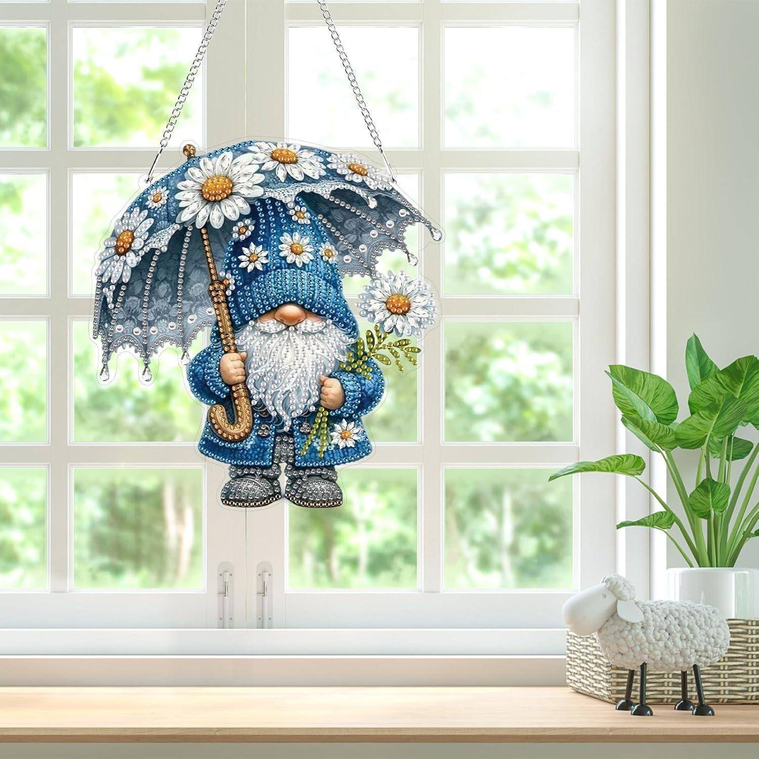 Eine blaue Zwergfigur hängt in einem Fenster, hält einen Regenschirm mit Blumenmuster und einen Blumenstrauß, während ein Topfpflanze und eine kleine Schaffigur auf der Fensterbank stehen.