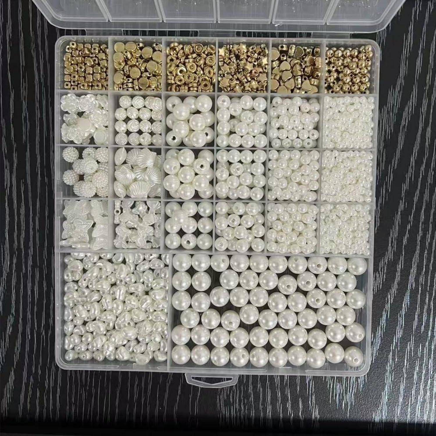 Offene Organizer-Box mit Fächern gefüllt mit sortierten perlenähnlichen Perlen und goldtonigen Abstandshaltern für die Schmuckherstellung.
