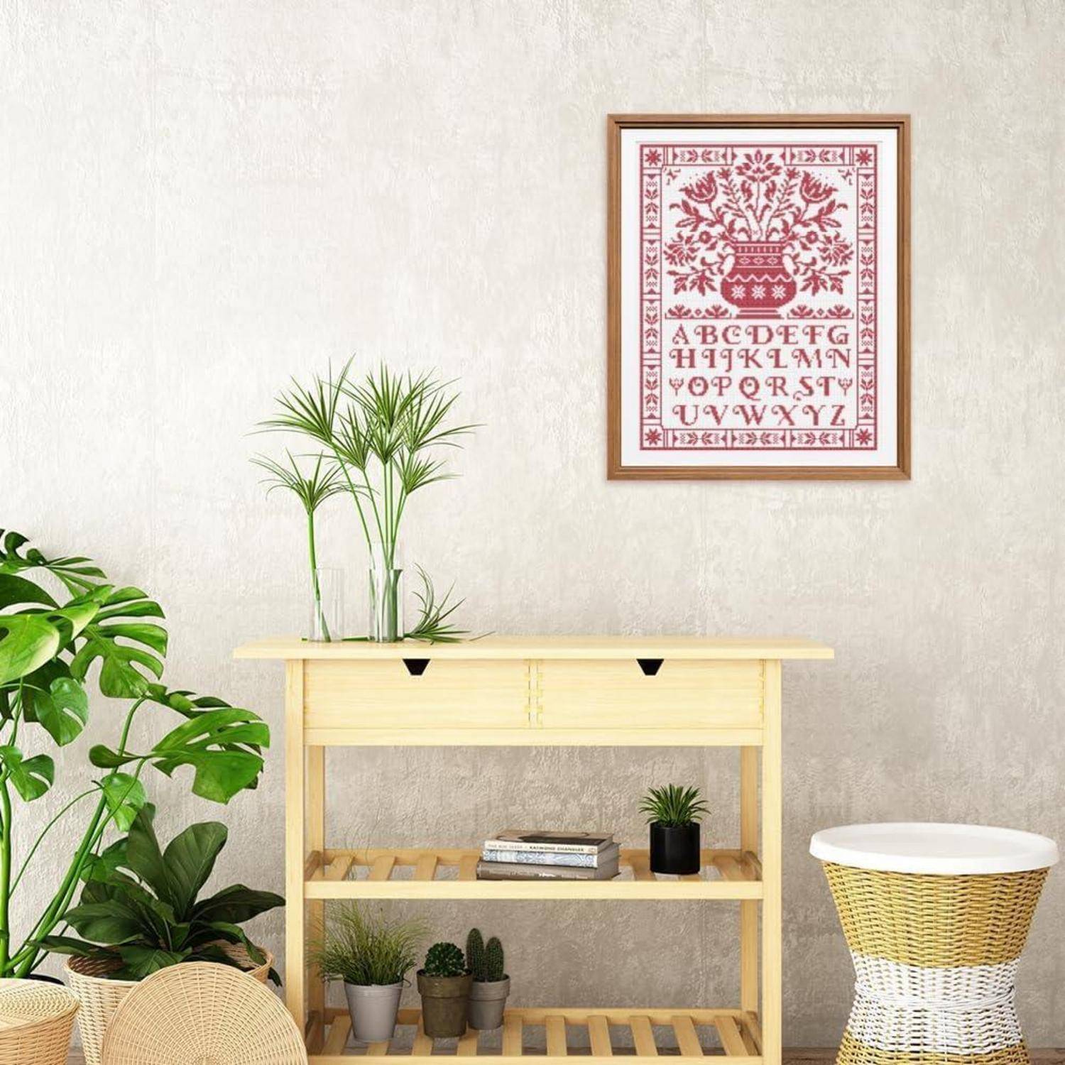 Helles Zimmer mit gerahmtem rotem botanischem Alphabet-Druck über einem Konsolentisch aus hellem Holz, auf dem Pflanzen und Bücher stehen, neben einem Korbtisch und Zimmerpflanzen.