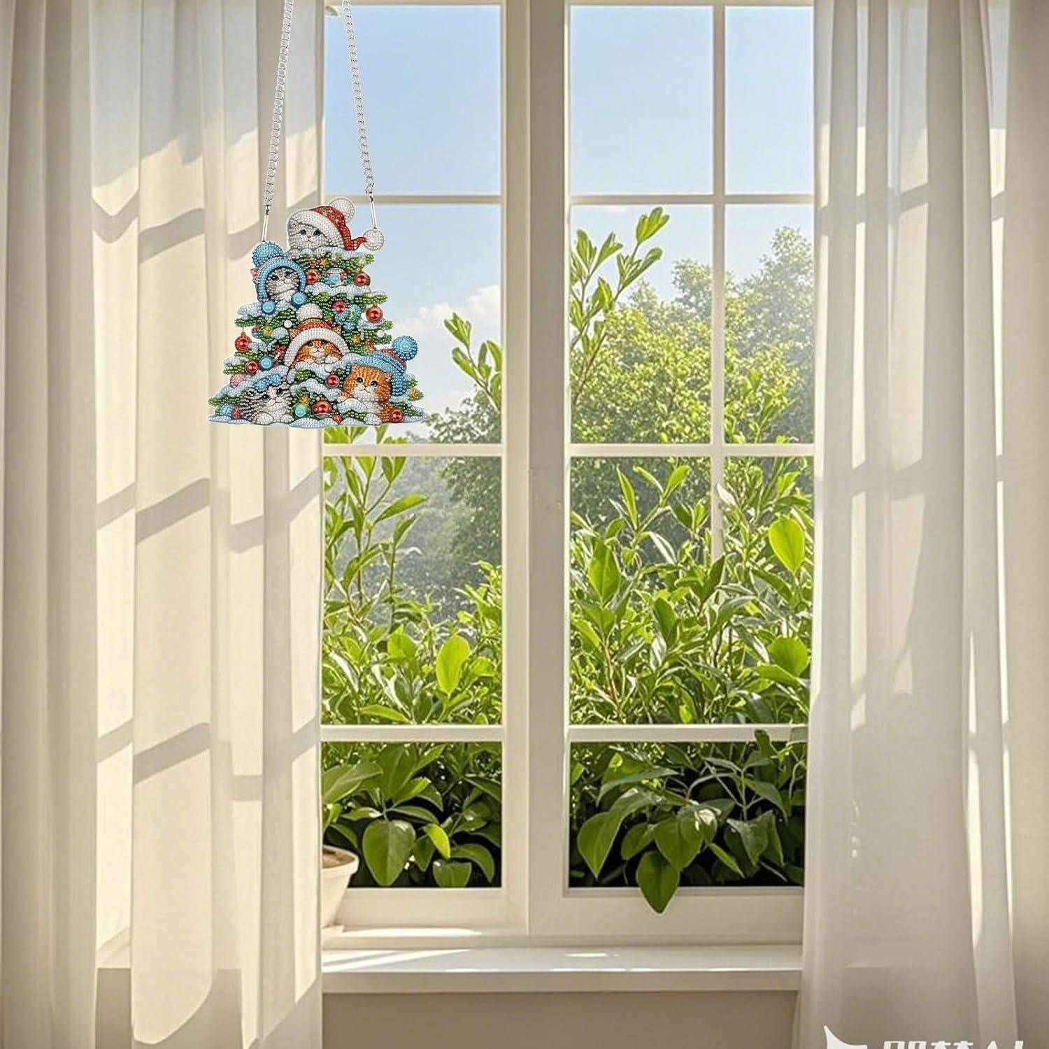 Sonniges Fenster mit weißen Gardinen und einem kleinen bunten hängenden Ornament, mit Blick auf üppige grüne Pflanzen draußen.