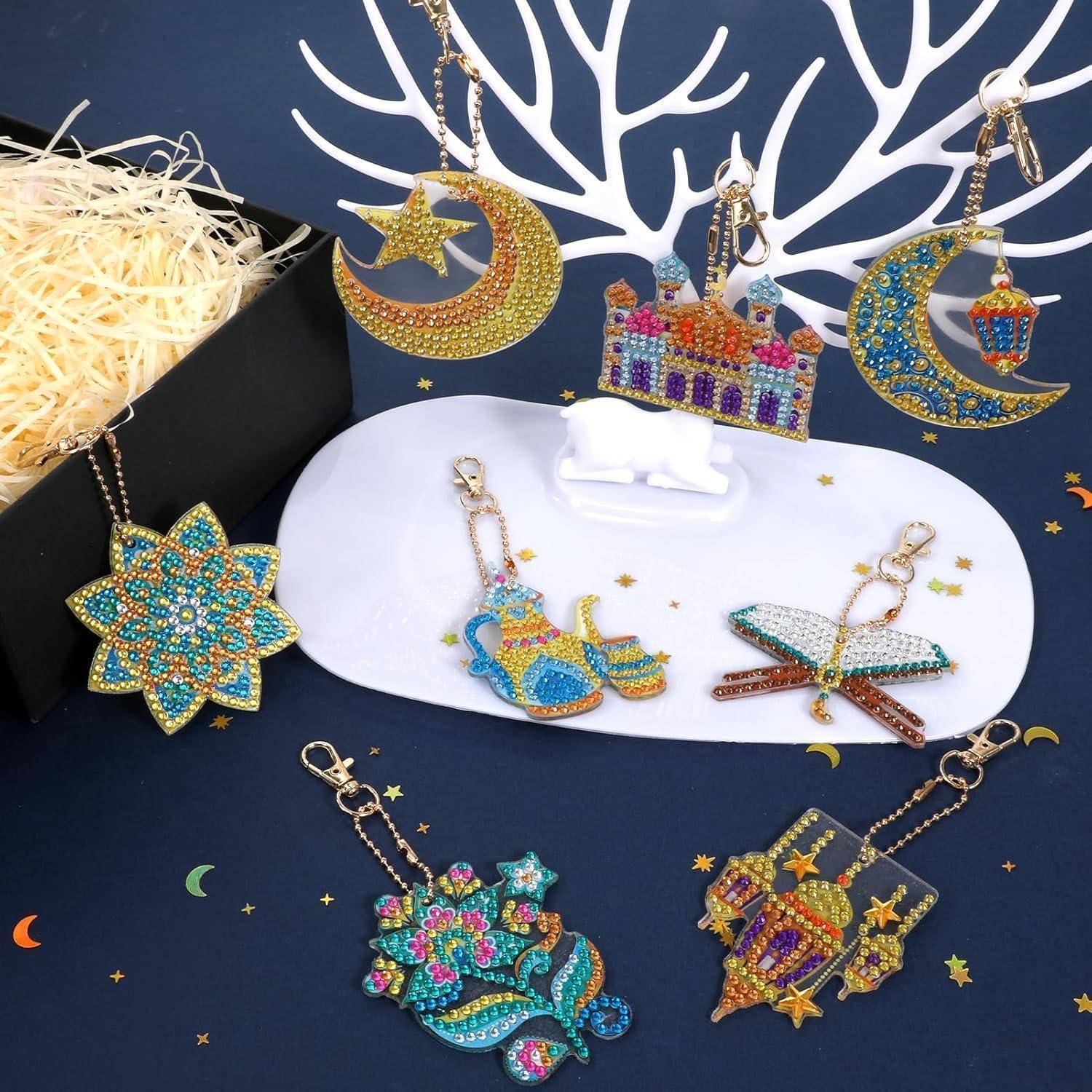 Dekorative verzierte islamische Ornamente und Schlüsselanhänger, darunter Mondsicheln, Sterne, Laternen und eine Moschee auf einem dunkelblauen Display.