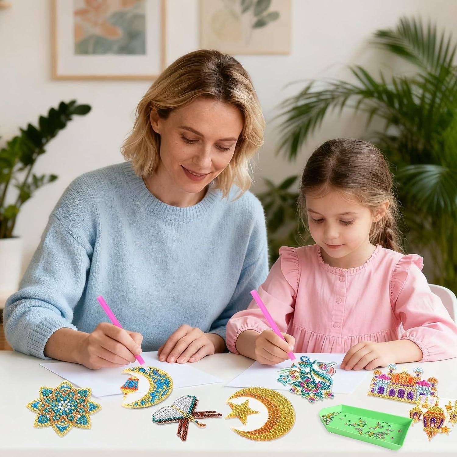 Eine Mutter und ihre kleine Tochter sitzen zusammen an einem Tisch und verzieren Handwerksstücke mit bunten Perlen oder Pailletten in einer hellen Wohnumgebung.
