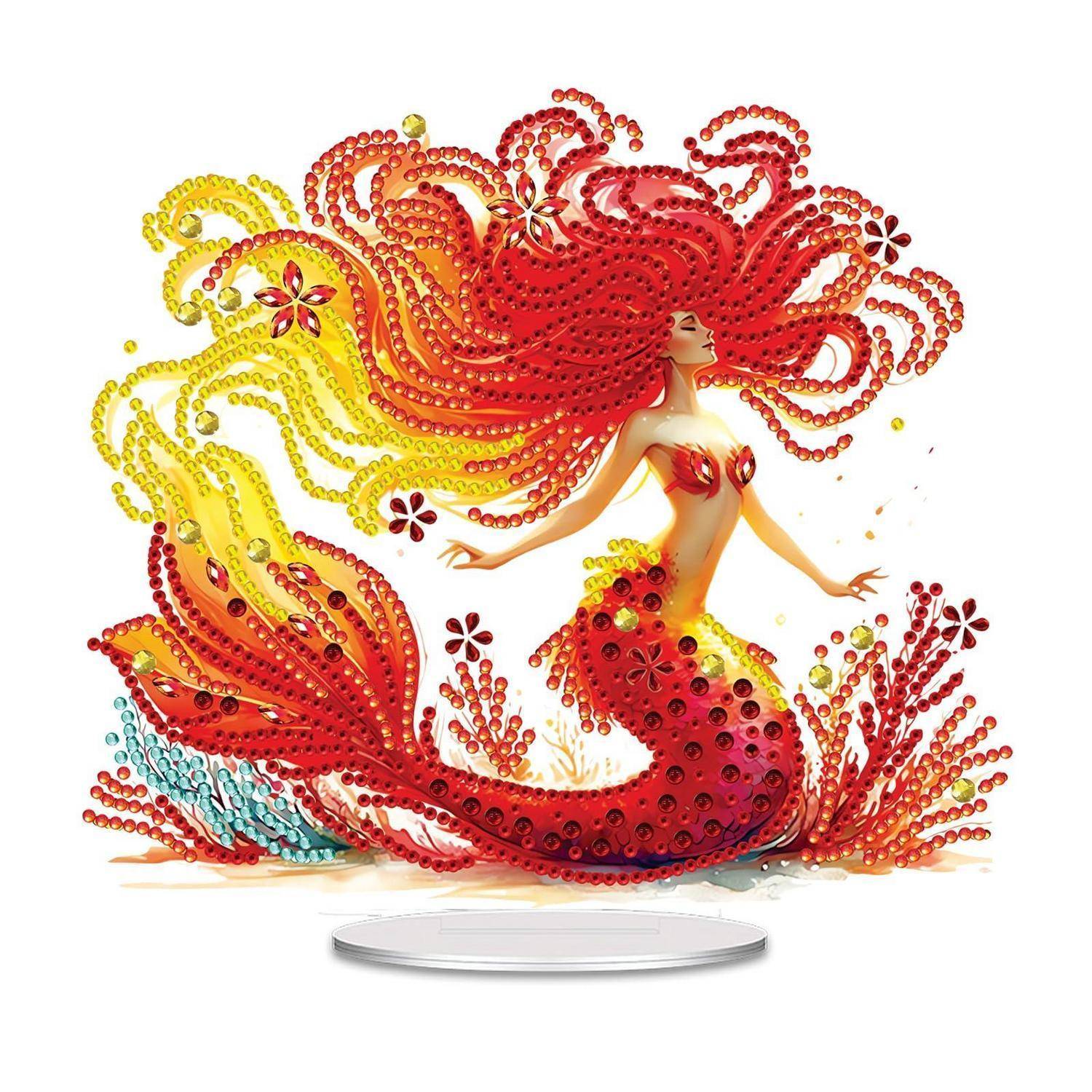 Eine geschmückte Meerjungfrau-Figur mit fließendem roten und gelbem Haar und einem rot-orangefarbenen Schwanz, in einer Pose auf einem kleinen runden Sockel.