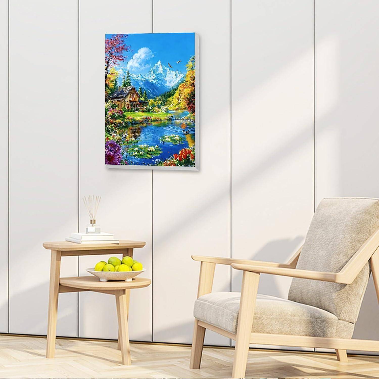 Ein farbenfrohes Landschaftsgemälde eines Bergsees hängt an einer weißen Wand über einem Beistelltisch und einem beigen Sessel in einem hellen, minimalistischen Zimmer.