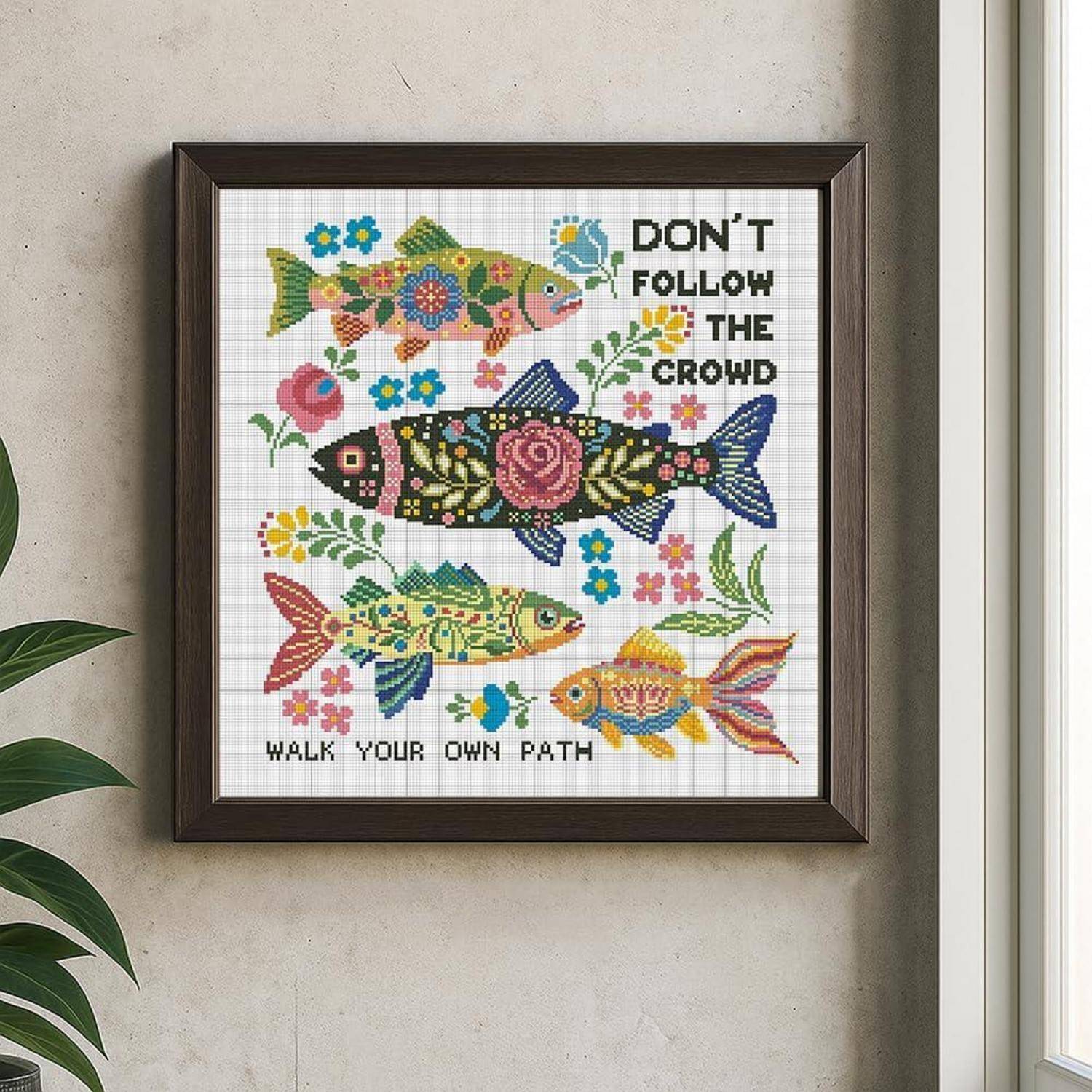 Gestickte Kreuzstichmotiv mit bunten Fischen, Blumen und den Worten „FOLGE NICHT DER MASSE