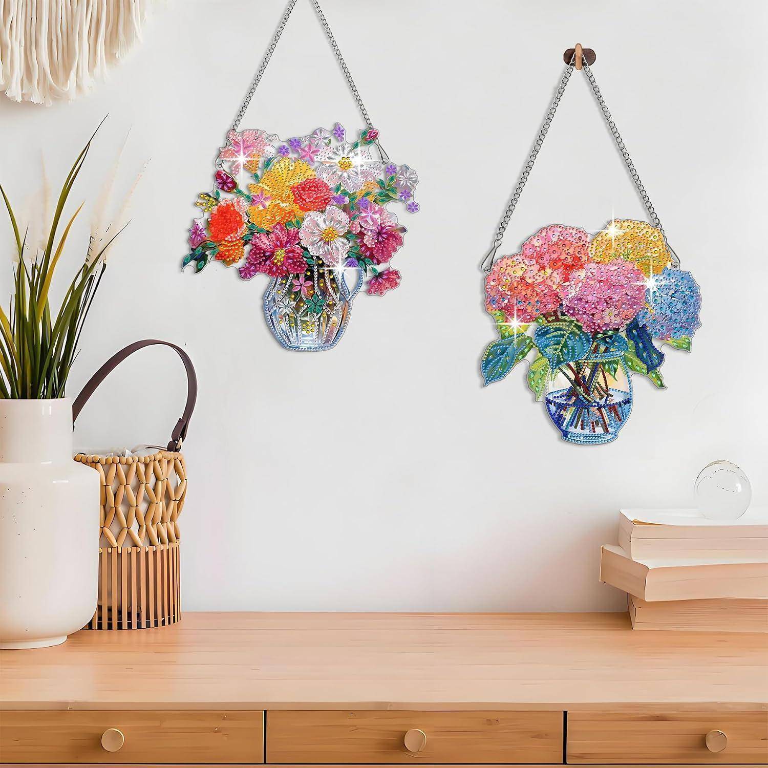 Zwei farbenfrohe hängende Blumenwanddekoration über einem Holzschreibtisch, mit einer Vase, einem Korb und gestapelten Büchern auf der Oberfläche.