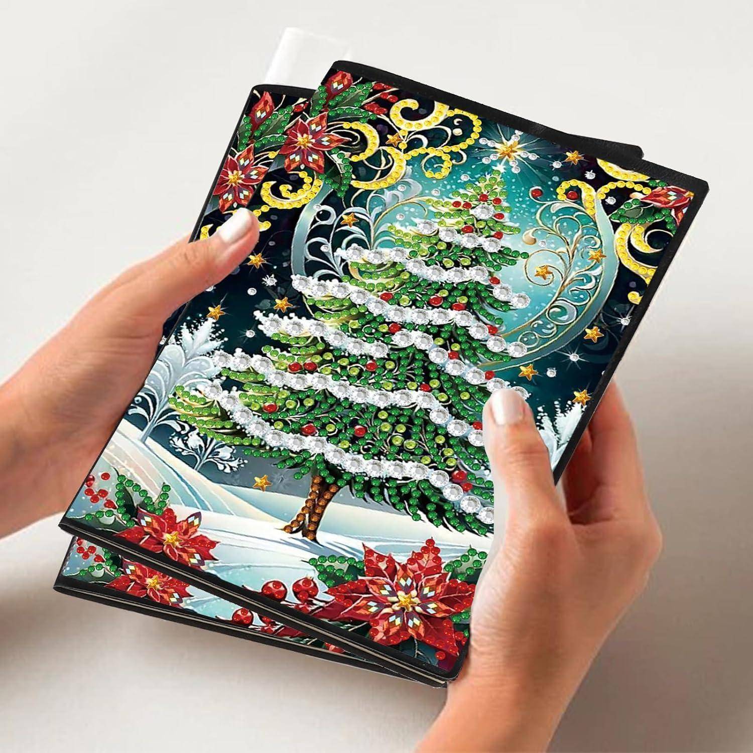 Hände halten ein dekoratives Notizbuch mit Weihnachtsbaumcover, das farbenfrohe edelsteinähnliche Ornamente, Schnee, Sterne und rote Weihnachtssterne zeigt.