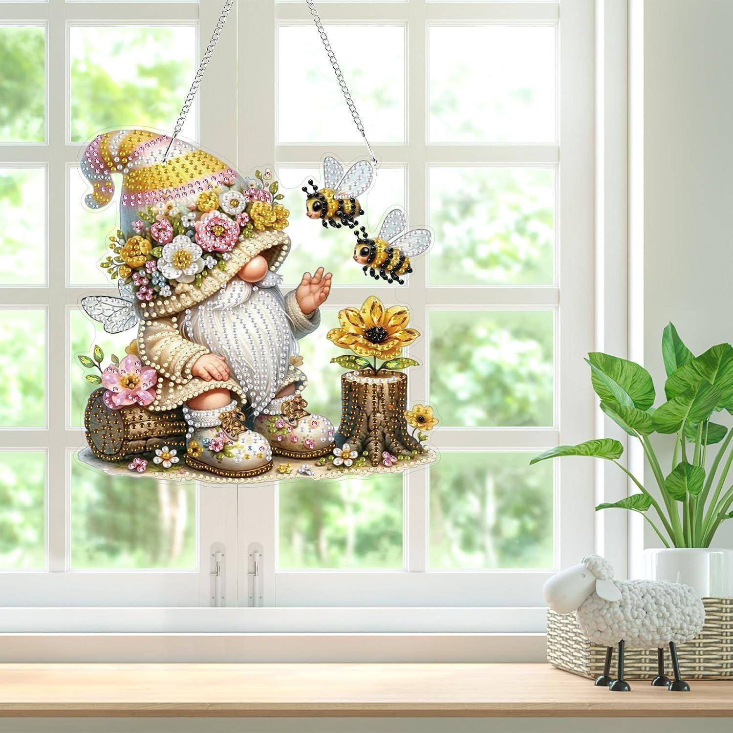 Verzierte Gnom-Fensterdekoration mit Blumen und Bienen, die vor einem hellen Fenster hängt, mit einer getopften Pflanze und einer kleinen Schaffigur auf der Fensterbank.