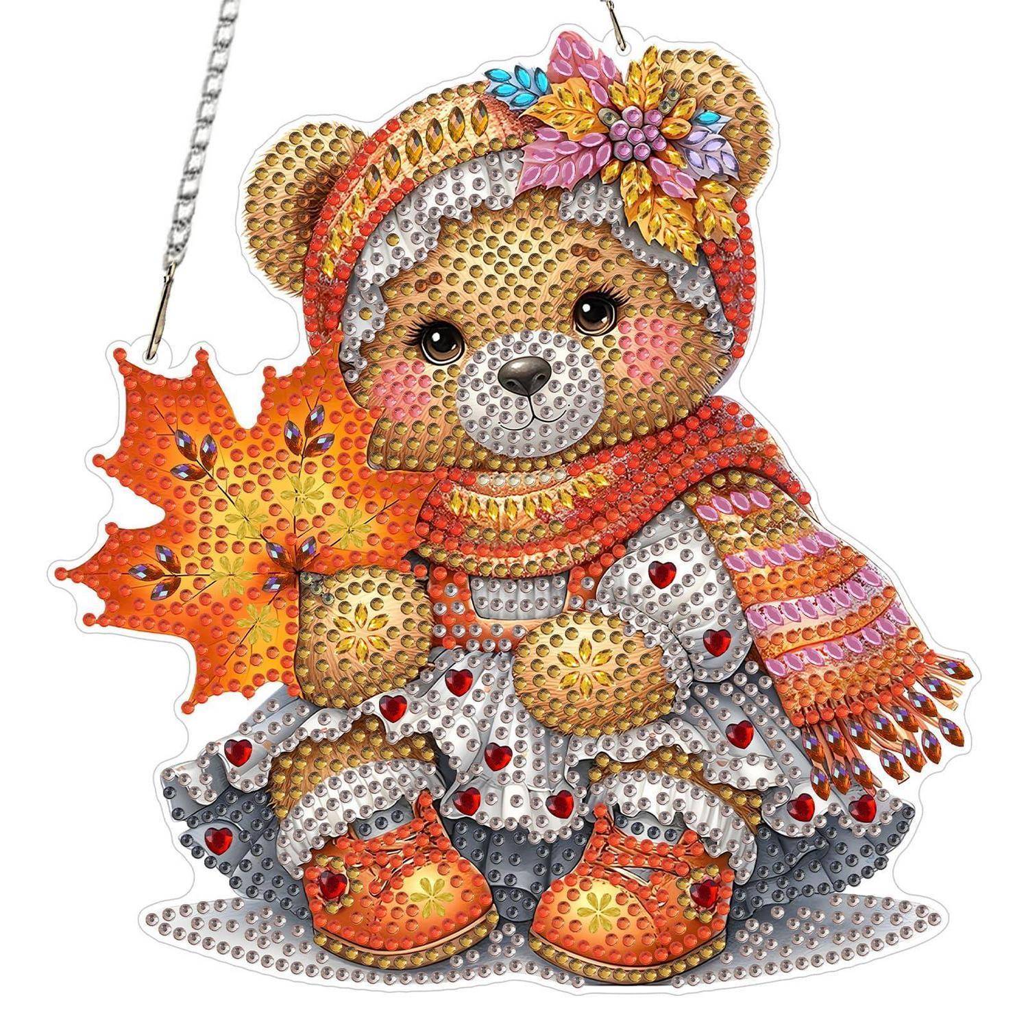 Ein glitzernder, mit Juwelen besetzter Teddybär-Schmuck, der ein orangefarbenes Herbstblatt hält, trägt einen gestreiften Hut und einen Schal.