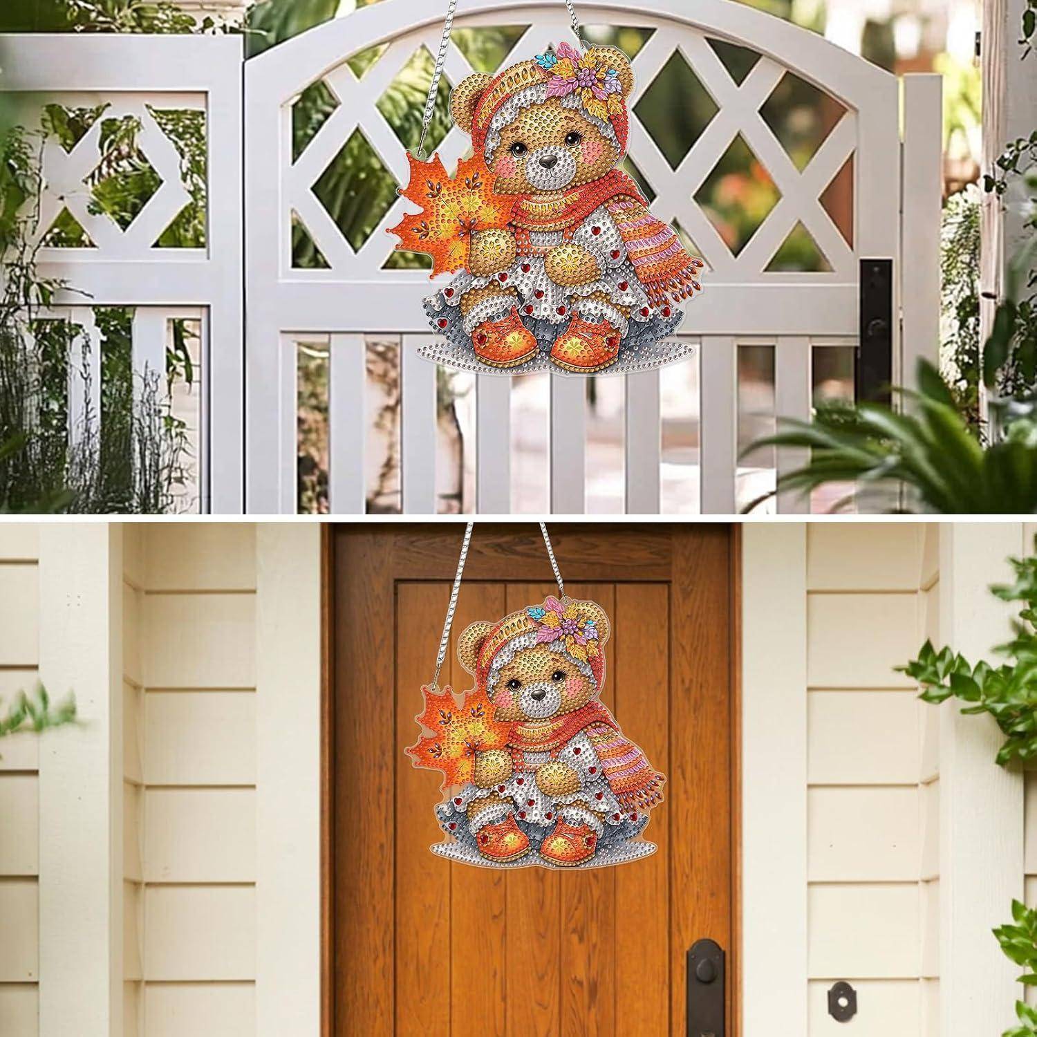 Perlenbestickter Teddybär als Herbstdekoration, der an einem weißen Gartengitter und einer hölzernen Haustür hängt.