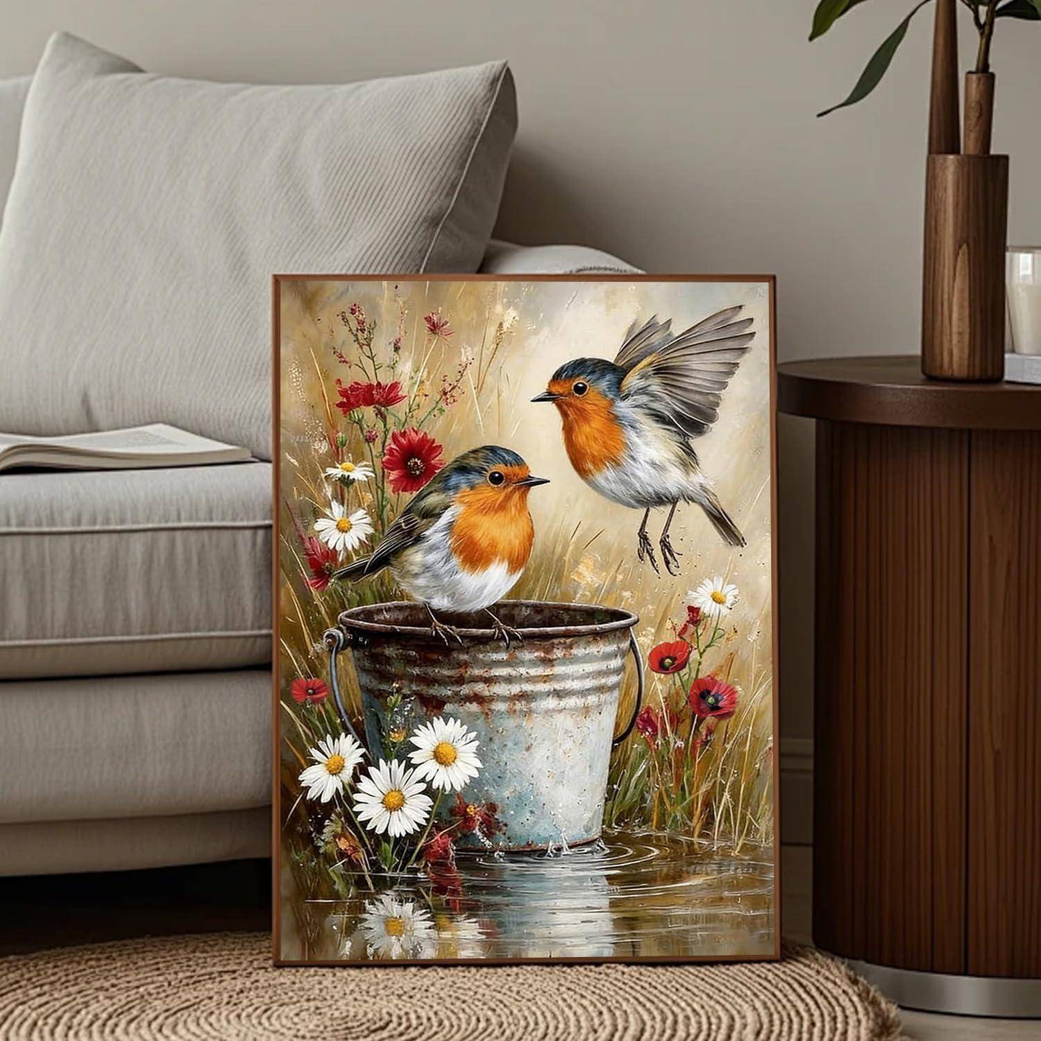 Gemälde mit zwei kleinen Vögeln, einer sitzt auf einem Metalleimer und einer fliegt über Wildblumen, ausgestellt auf dem Wohnzimmerboden neben einem Sofa und einem Beistelltisch.