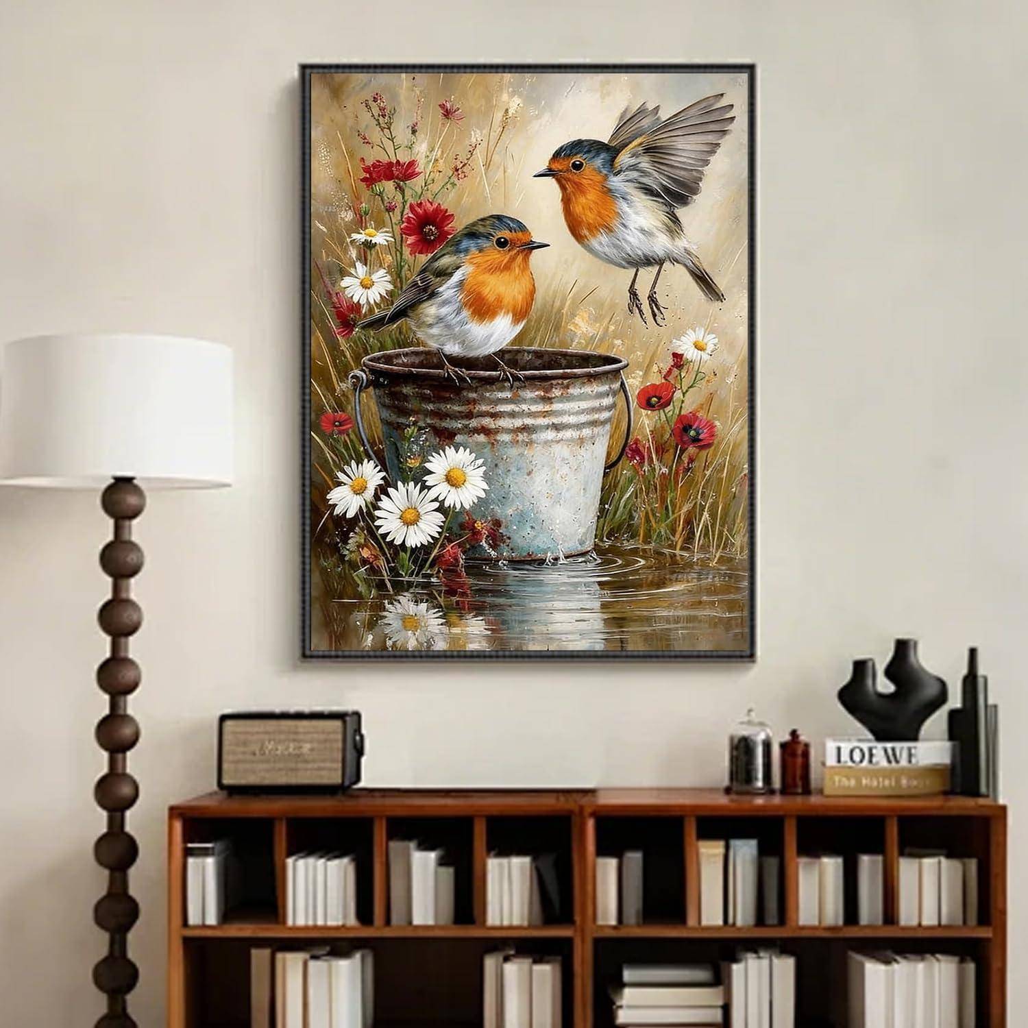 Gerahmtes Gemälde von zwei Rotkehlchen zwischen Gänseblümchen, eines in einem rostigen Eimer und eines über dem Wasser fliegend, hängend über einem Bücherregal mit einer Lampe daneben.