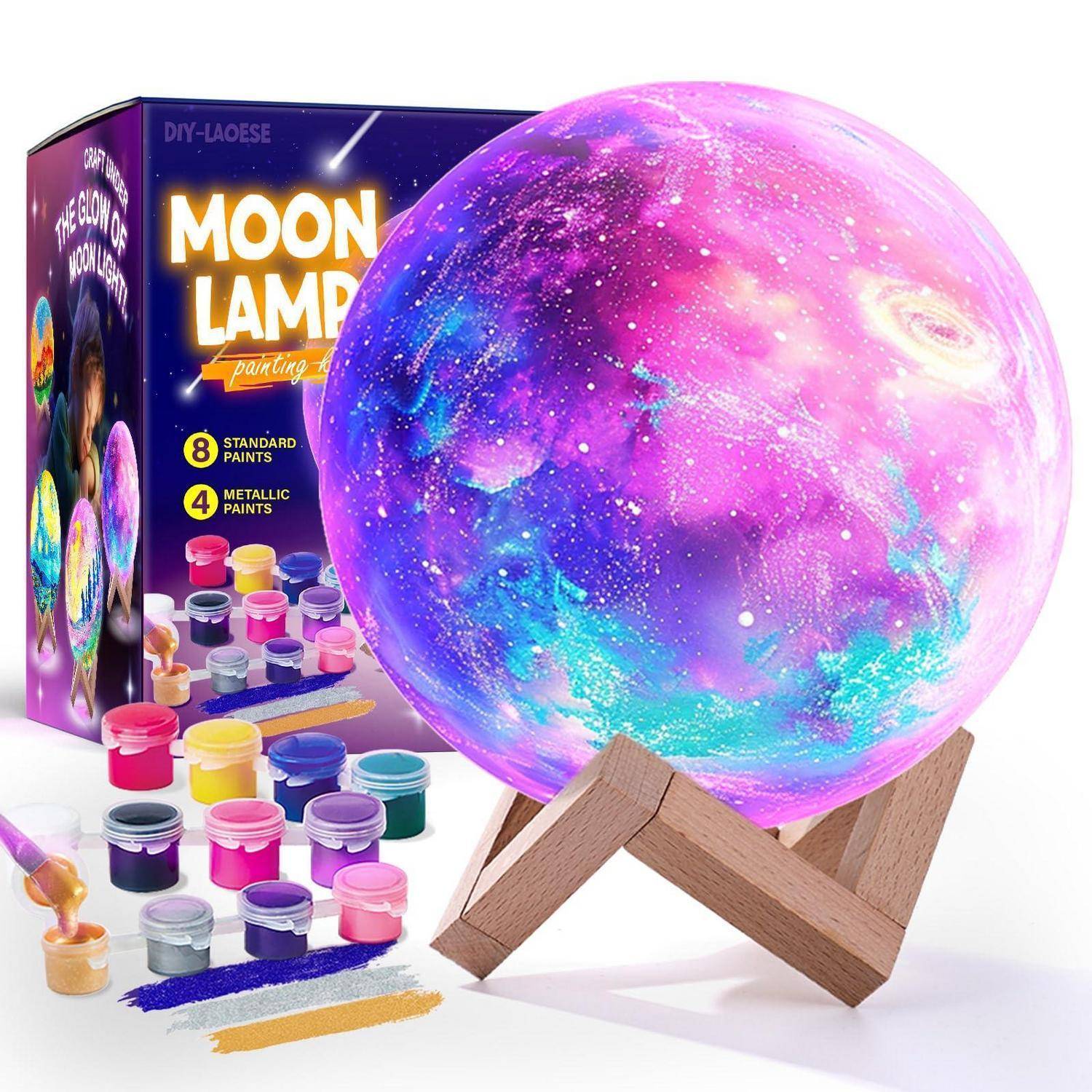 Bemalte Mondlampen-Bastelset mit leuchtender rosa-violett-blauer Kugel auf Holzständer, Farbdosen, Pinseln und Schachtel mit der Aufschrift „MOON LAMP painting