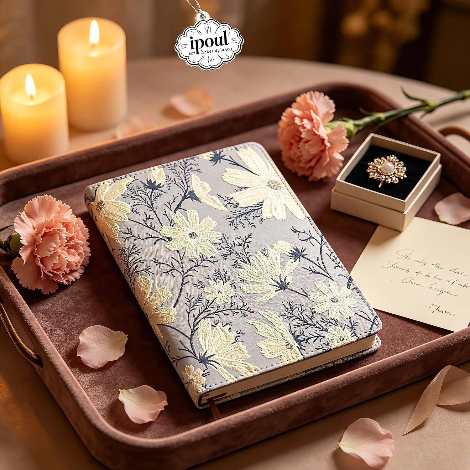 Notizbuch mit Blumenmuster auf einem Tablett mit Kerzen, Nelken, einer Ringschachtel und einem handgeschriebenen Zettel, angeordnet als Geschenkdisplay.