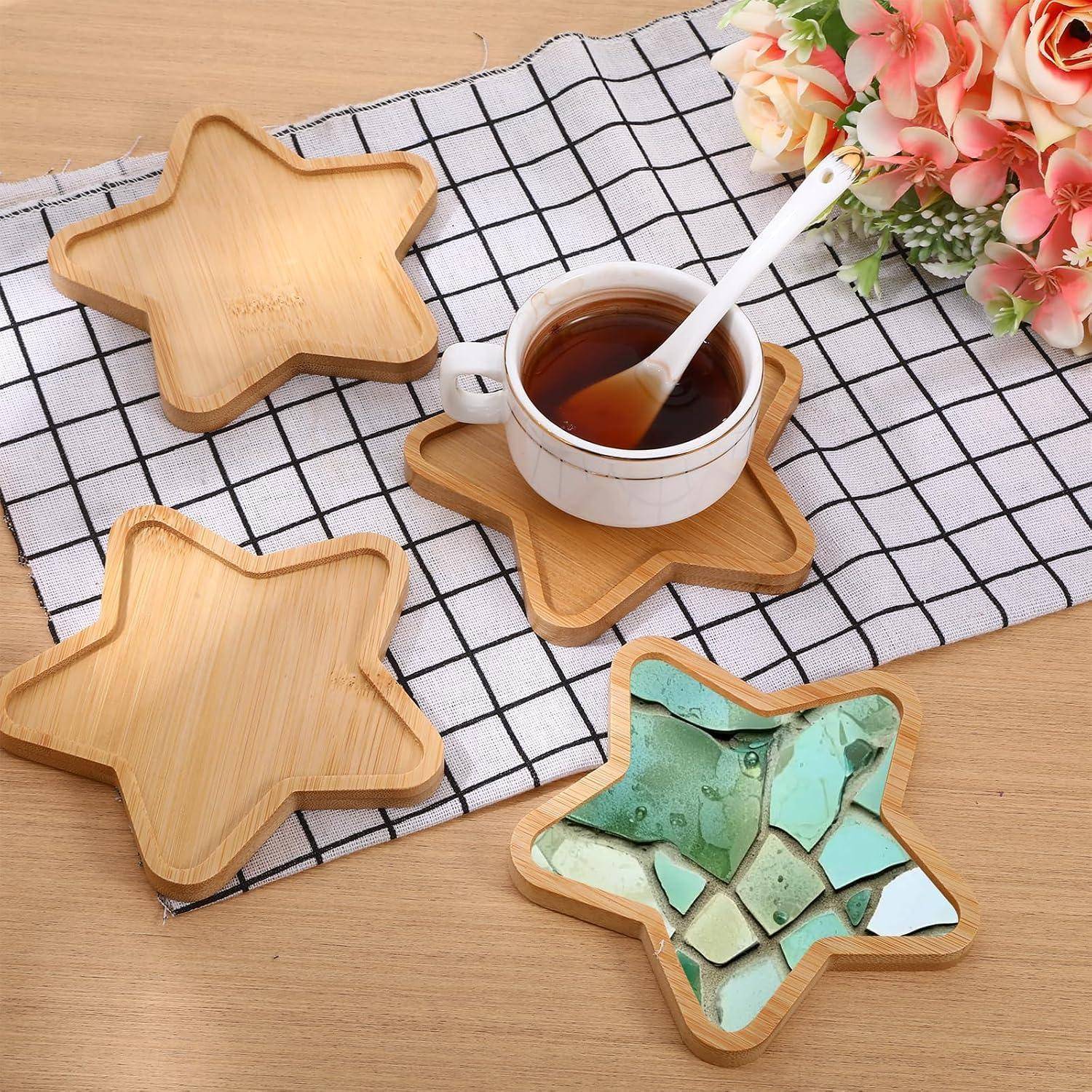 Sternförmige Bamboo-Untersetzer auf einem karierten Tuch, einer hält eine Tasse Tee und einen Löffel, mit rosa Blumen in der Nähe.