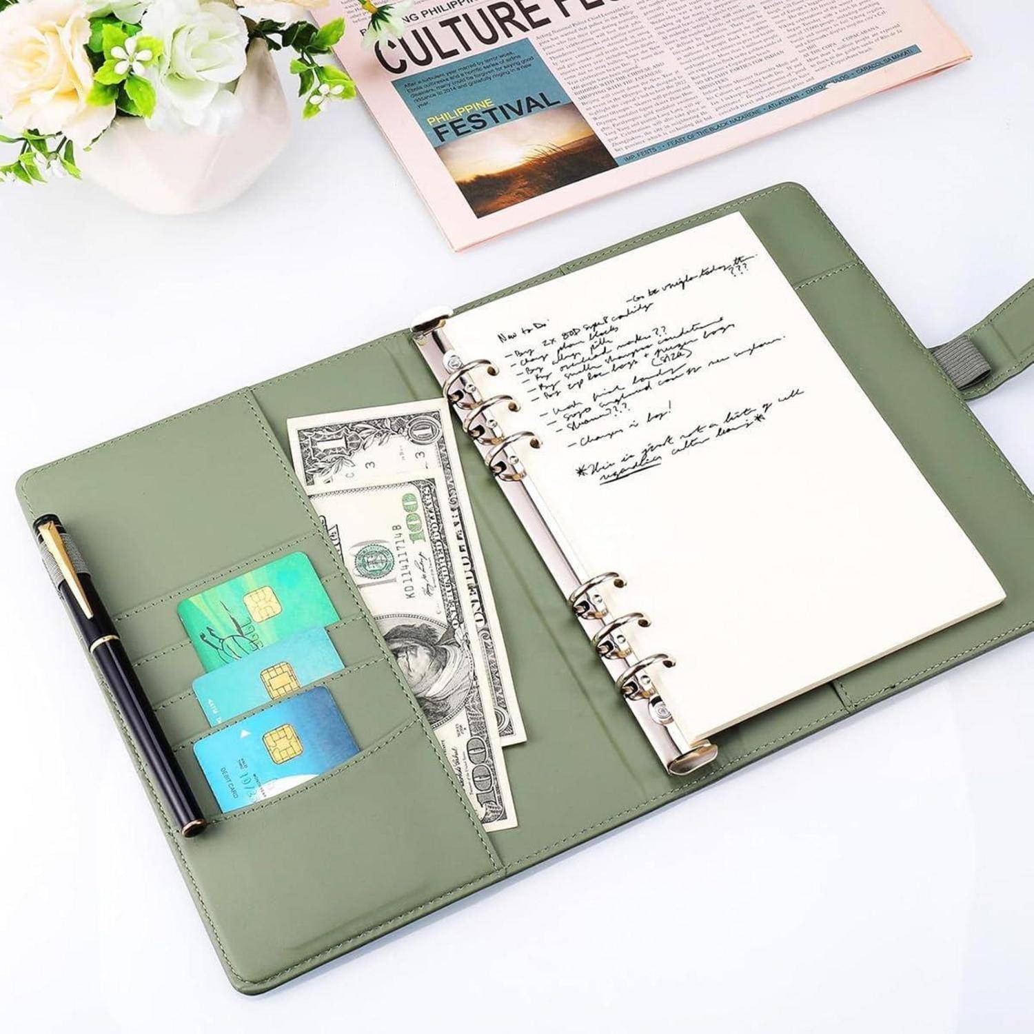 Offener grüner Ringordner-Planer mit Taschen für Karten und Bargeld, ein Stift auf der linken Seite und eine handschriftliche Notizseite auf der rechten Seite.