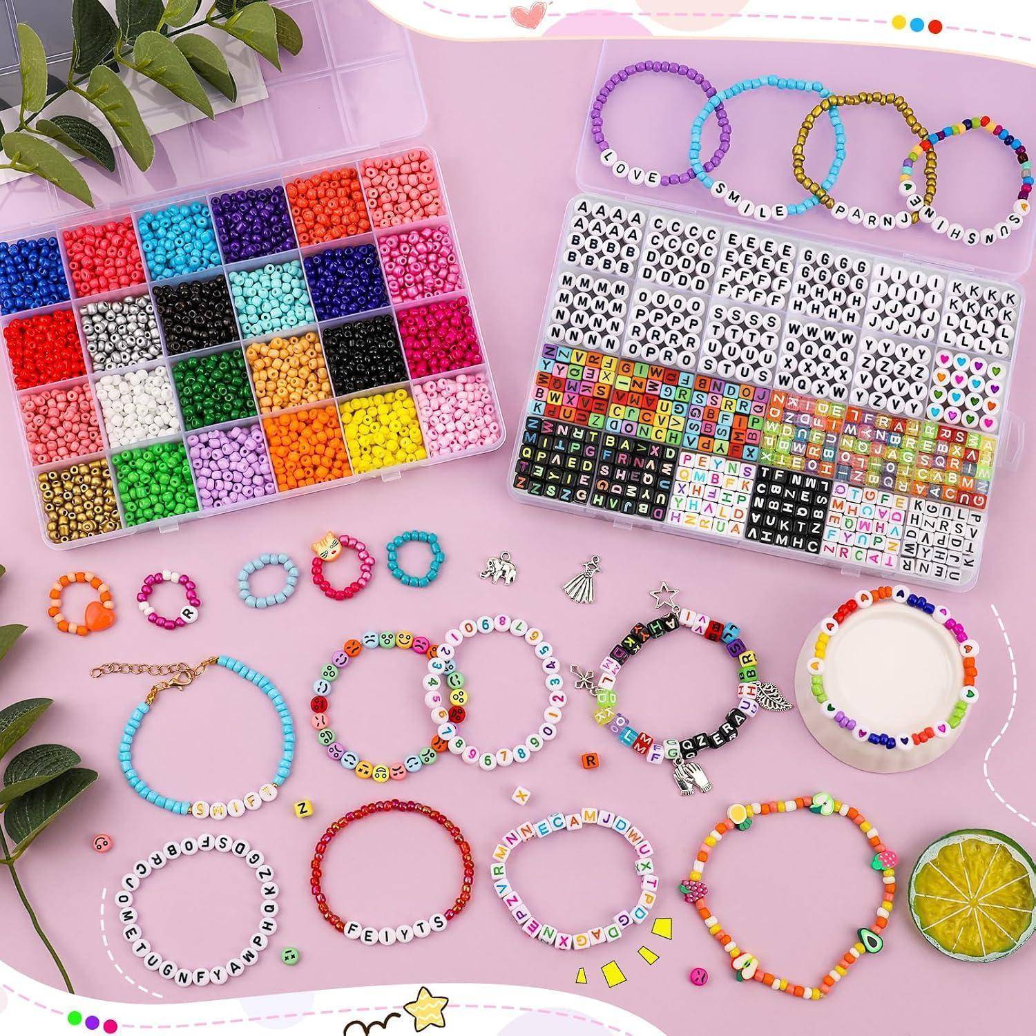 Szene des Perlenschmuckhandwerks mit Tabletts farbiger Perlen und Buchstabenperlen, plus fertige Armbänder und Namensbänder, die auf einer rosa Oberfläche angeordnet sind.