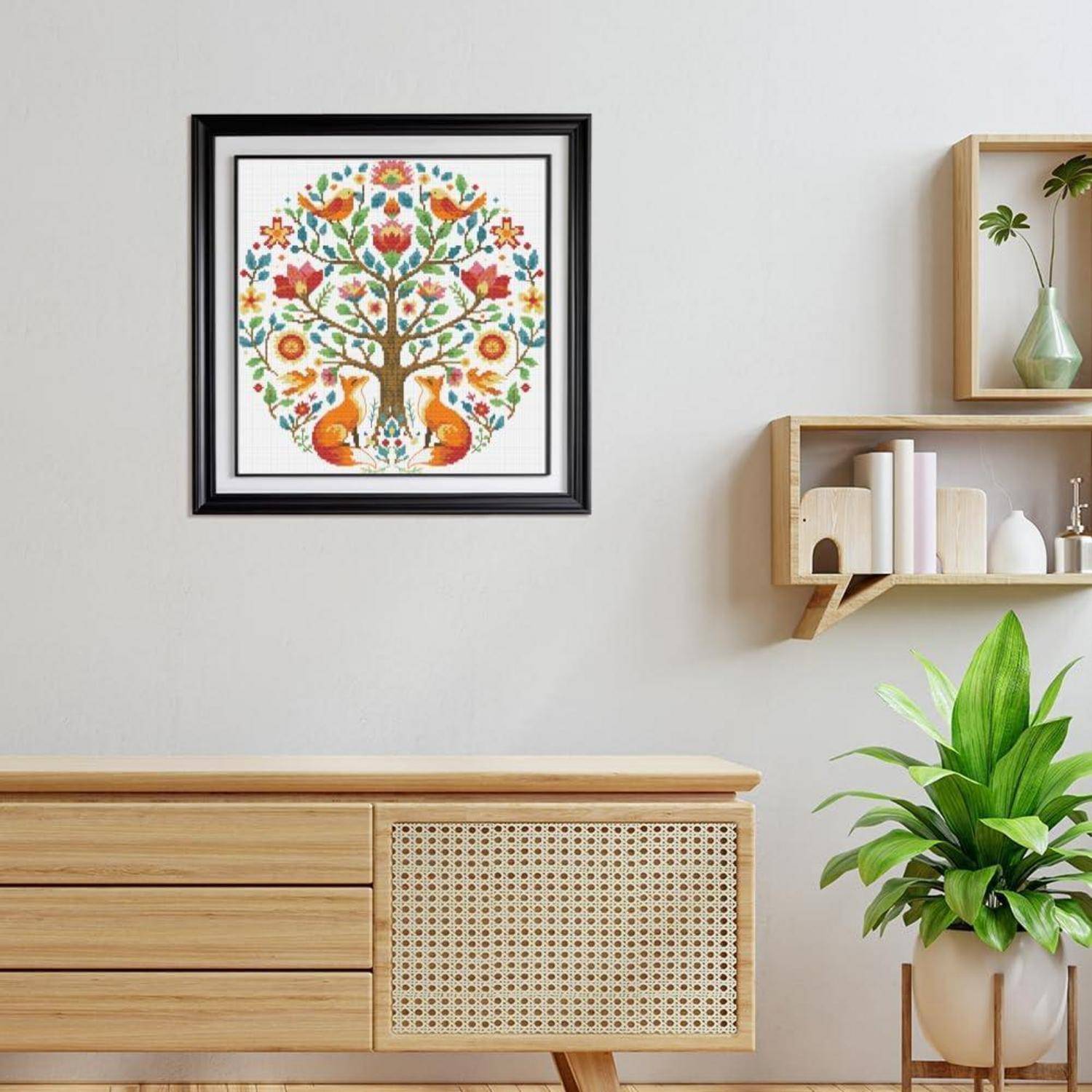 Rahmengebundenes buntes Baum-Kunstwerk hängt über einem Holzschrank in hellem Ton in einem minimalistischen Raum mit Regalen und einer Topfpflanze.