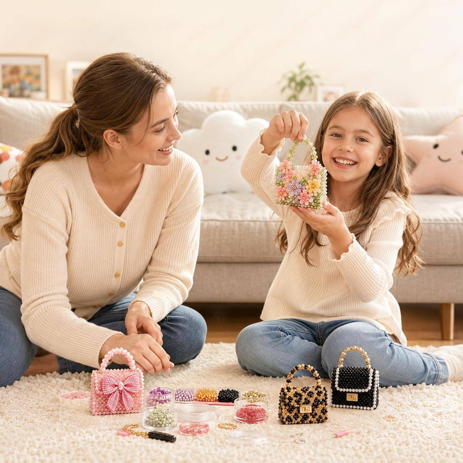 Lächelndes Mädchen zeigt eine perlenbesetzte kleine Handtasche, die es hergestellt hat, während es mit einer erwachsenen Frau auf dem Wohnzimmerboden sitzt, mit Bastelperlen und zwei fertiggestellten Taschen in der Nähe.
