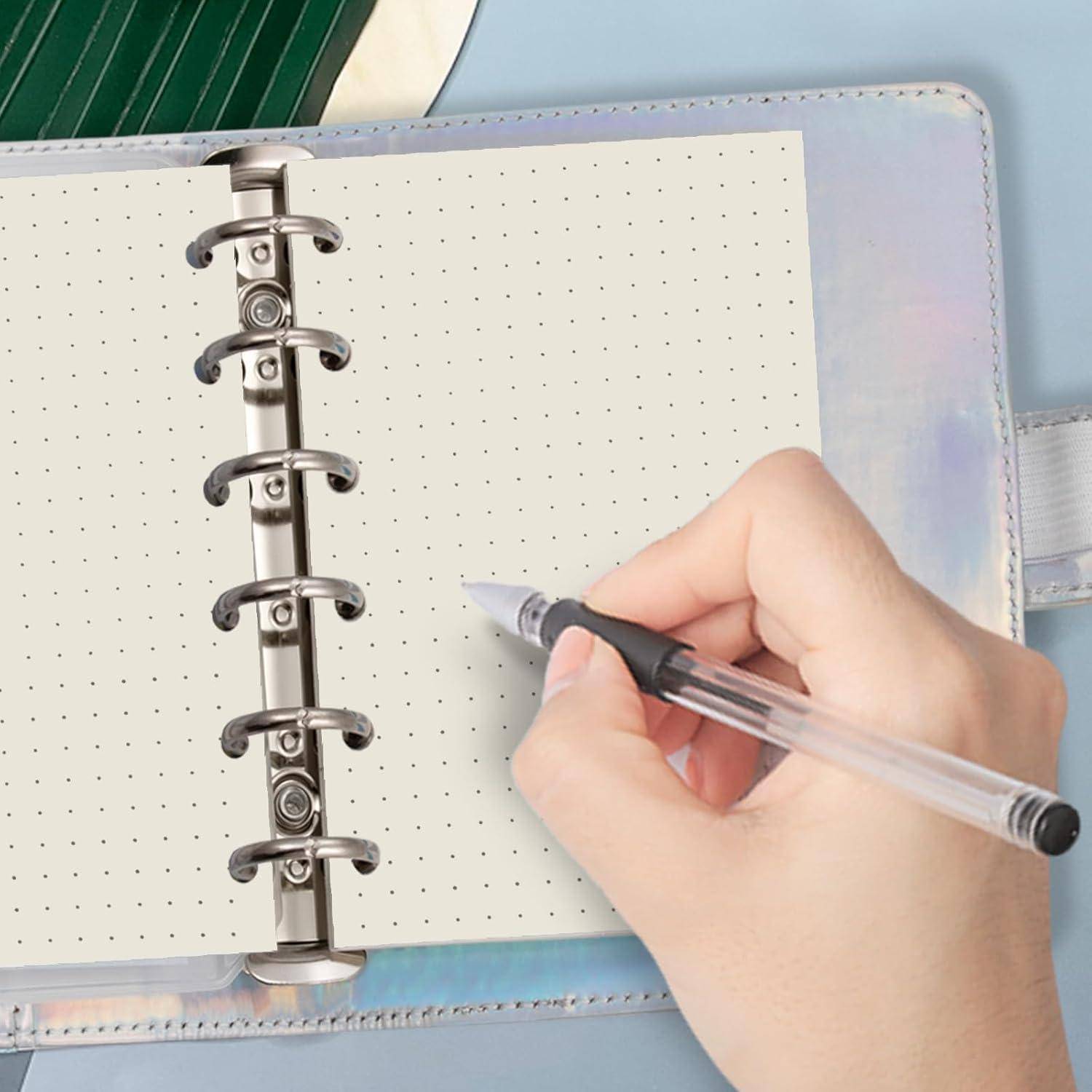 Hand hält einen Stift über einem offenen Notizbuch mit Punkten in einem Ringbinder, bereit zum Schreiben oder Planen.