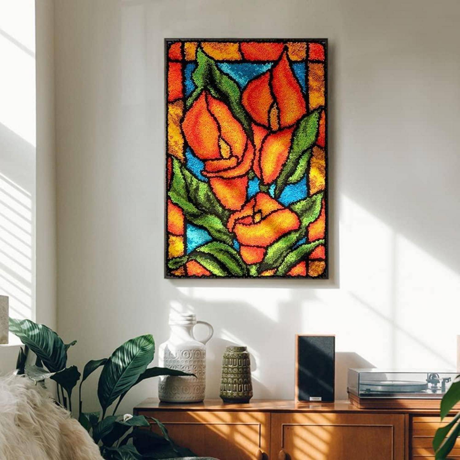 Gerahmte Bleiglasfenster-Kunstwerk im Blumenstil mit orangefarbenen Blüten und grünen Blättern hängt über einer Holzkommode in einem sonnendurchfluteten Zimmer.