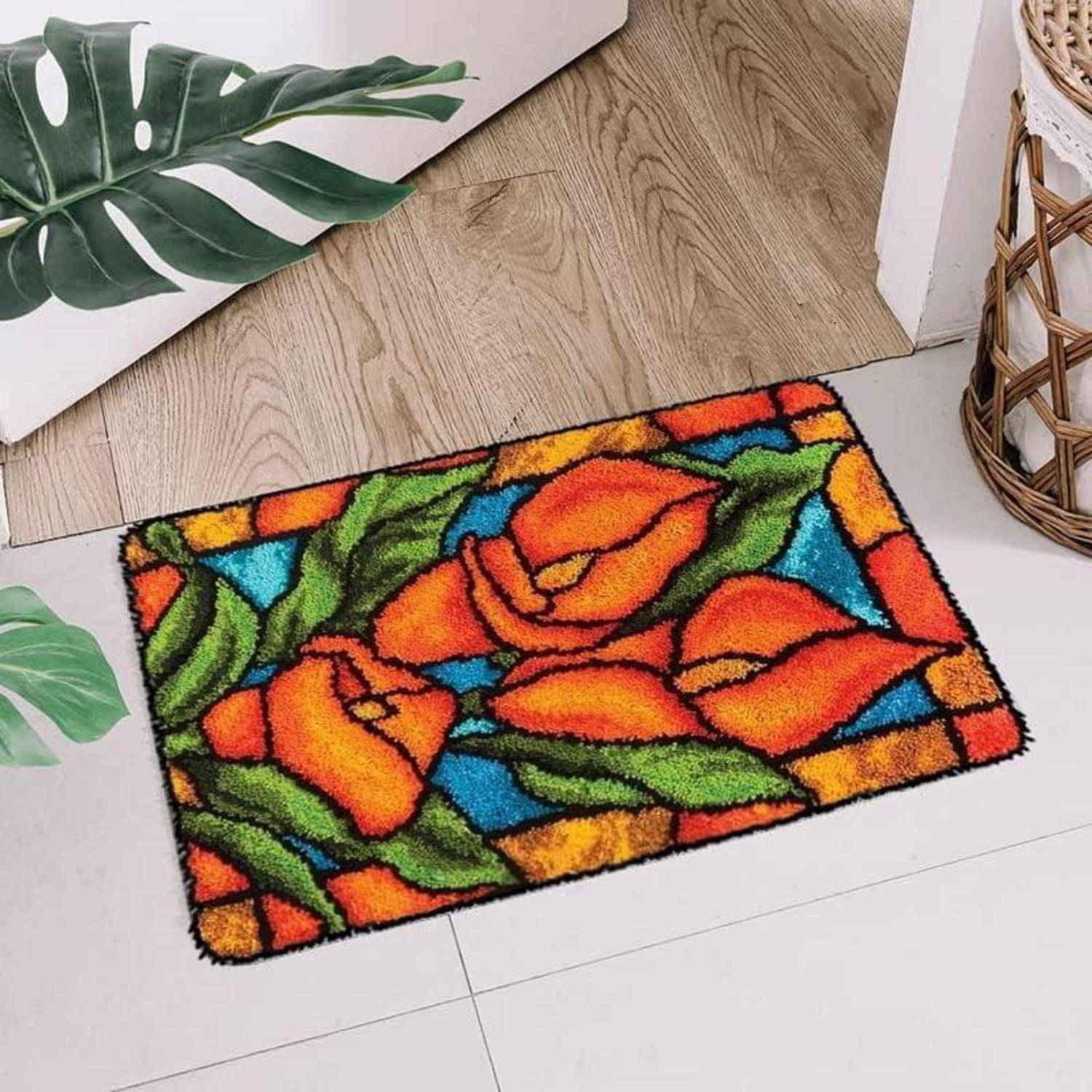Bunte Blumen-Fußmatte mit orangefarbenen Blüten und grünen Blättern, platziert auf einem hellen Boden neben einem Weidenkorb und Zimmerpflanzen.