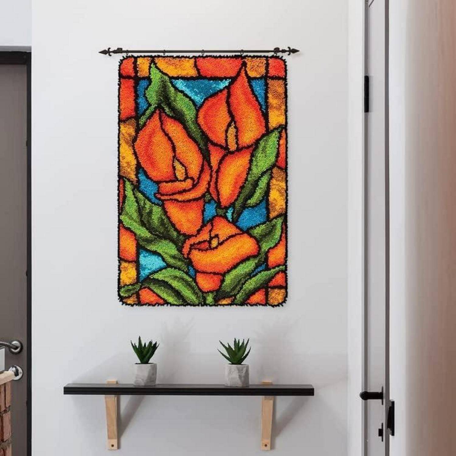 Farbenfrohe Wandkunst im Buntglasstil mit orangefarbenen Rosen und grünen Blättern hängt über einem schmalen Regal, das zwei kleine Topfpflanzen hält.